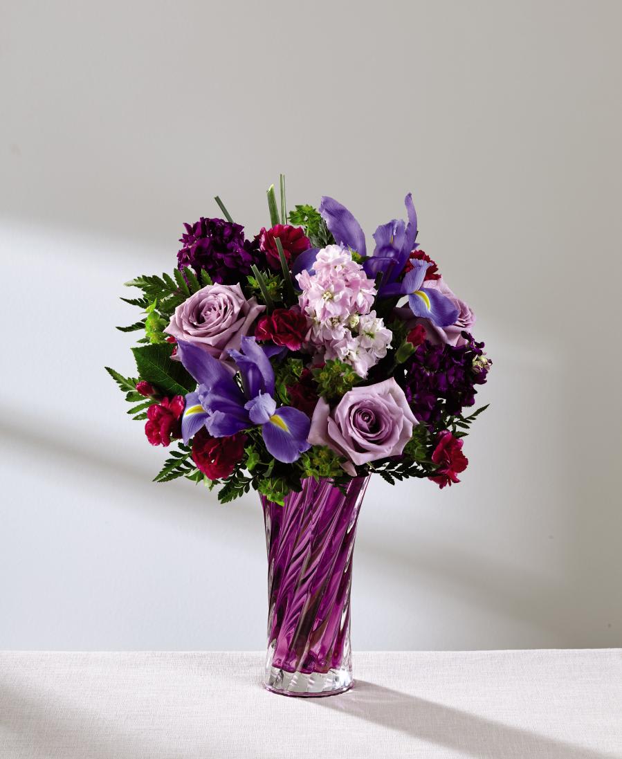 The FTD Spring Garden Bouquet - Deluxe - Feel the pull of purple this spring season with this gorgeous flower bouquet! Lavender roses and daisies bring a sense of light to this arrangement surrounded by the deeper shades of purple iris, fuchsia mini carnations, purple gilly flower, pink gilly flower, and bupleurum. Presented in a swirling purple glass vase that takes the styling of this flower bouquet to a whole new level, this arrangement is the perfect way to delight your mom this coming Mother's Day, or send your sweetest spring wishes in honor of Easter or a special birthday. GOOD bouquet includes 9 stems. Approx. 16"H x 11"W. BETTER bouquet includes 11 stems. Approx. 17"H x 11"w. BEST bouquet includes 15 stems. Approx. 18"H x 15"W. EXQUISITE bouquet includes 18 stems. Approx. 19"H x 15"W.