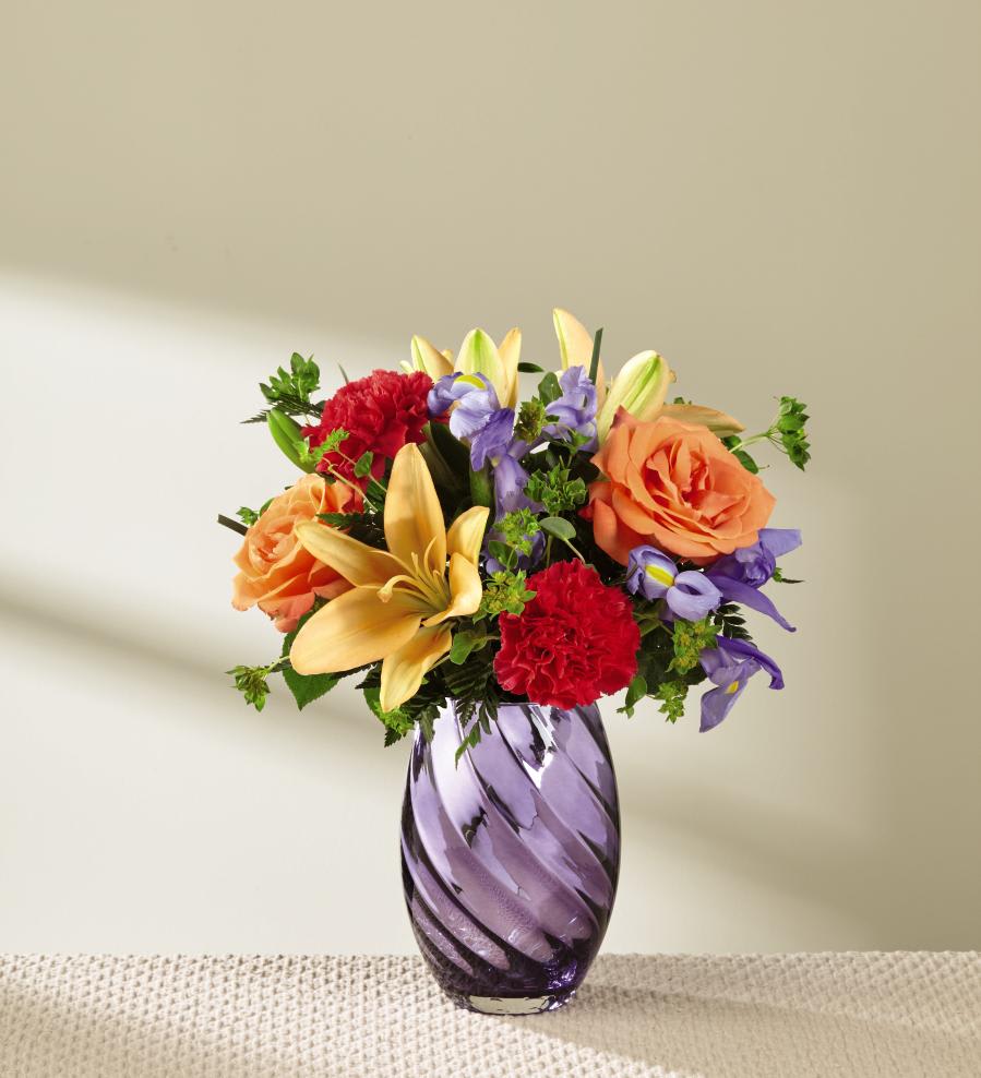 The FTD Make Today Shine Bouquet - Reflecting light and color with it's sheer radiance and exquisite design, this stunning spring bouquet is ready to make your recipient's day truly shine! Offering a bold array of seasonal hues, this arrangement brings together orange roses and peach Asiatic Lilies offset by blue iris, fuchsia carnations, lavender monte casino asters, and bupleurum stems. Presented in a gorgeous keepsake lavender glass vase with a silver metallic finish to catch the eye and a swirling design pattern that gives it even further interest and detail, this flower arrangement is set to create an incredible birthday, thinking of you, or congratulations gift. GOOD bouquet includes 8 stems. Approx. 13"H x 11"W. BETTER bouquet includes 12 stems. Approx. 15"H x 12"W. BEST bouquet includes 16 stems. Approx. 16"H x 13"W. EXQUISITE bouquet includes 20 stems. Approx. 16"H x 14"W.