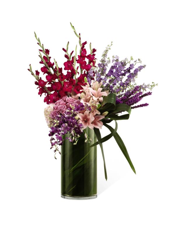 FTD Whispering Love Arrangement - The FTD Whispering Love Arrangement is an exquisite display of   limitless beauty that is a blooming tribute to the life of the deceased.   Lavender roses, magenta gladiolus, purple mokara orchids, purple   trachelium, pink bouvardia, and pink hydrangea blooms are accented by   lush greens and arranged in a clear glass cylinder lined with ti leaves   to create a moving presentation that exudes love, warmth and comfort at   their final memorial service.      40âh x 32âw