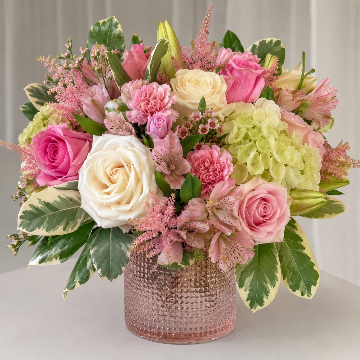 Simple &amp; Sweet Romance Tampa Bay  - A lush round bouquet of pink and white roses accented with pale green hydrangea creates the first impression-an immediate, romantic message perfect as an anniversary roses arrangement or a birthday bouquet for someone who loves soft pastels. The textured blush glass vase gives the arrangement a polished, feminine finish that reads as both celebratory and quietly elegant, making it a lovely choice for spring gifting or to say "I'm thinking of you" in a meaningful way.  This Simple &amp; Sweet Romance Tampa Bay design mixes pink carnations, soft alstroemeria, and a few lily buds for added texture and gentle fragrance, layered with variegated greenery to enhance the garden-style, full-rounded shape. The color story-pink, white, green and a hint of yellow-keeps the look light and airy, while the textured pink glass vase ties the palette together and serves as a decorative keepsake.  Ideal for mothers, partners, close friends, or anyone who appreciates romantic, feminine florals, this arrangement arrives ready to display in its vase and brightens a room with soft color and natural texture. For best longevity, place away from direct heat and change the water every other day to keep blooms looking fresh.