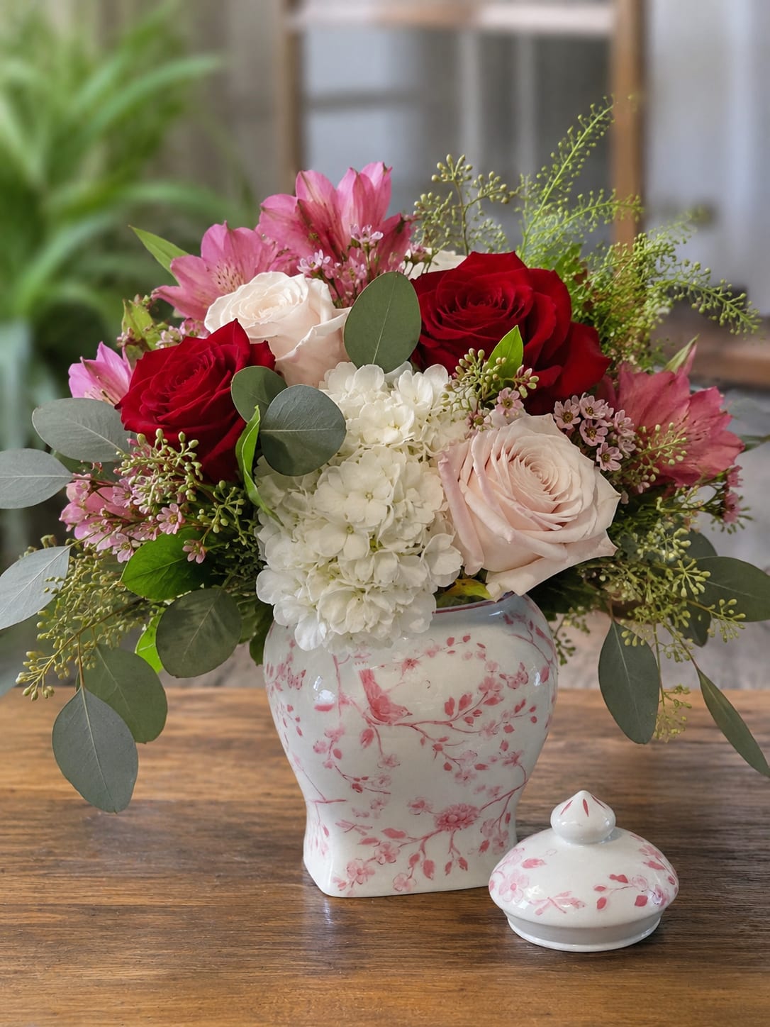 Elegant &amp; Timeless for Tampa Bay  - Deep red and blush roses meet a cloud of white hydrangea and pink alstroemeria in a romantic anniversary or birthday bouquet that reads both elegant and timeless. This flower arrangement for Tampa Bay opens with rich, layered color-red for passion, blush for tenderness-so the person you're thinking of will feel celebrated and truly seen, whether for Mother's Day, an anniversary, or just because.  The design is lush and rounded, arranged in a round white ceramic vase decorated with soft pink blossom patterns and accompanied by a matching ceramic lidded piece for a coordinated keepsake. Eucalyptus-like foliage and airy filler branches give the bouquet a soft garden texture; the mix of roses, hydrangeas, alstroemeria, and greenery creates depth, movement, and a pleasing contrast of full blooms and delicate accents.  Perfect for marking milestone moments or brightening someone's day, this arrangement arrives ready to display and doubles as a decorative ceramic container once the blooms have faded. For best longevity, keep in a cool spot away from direct sun and refresh the water every couple of days; choose the size that fits your sentiment to ensure the right impact for your recipient.
