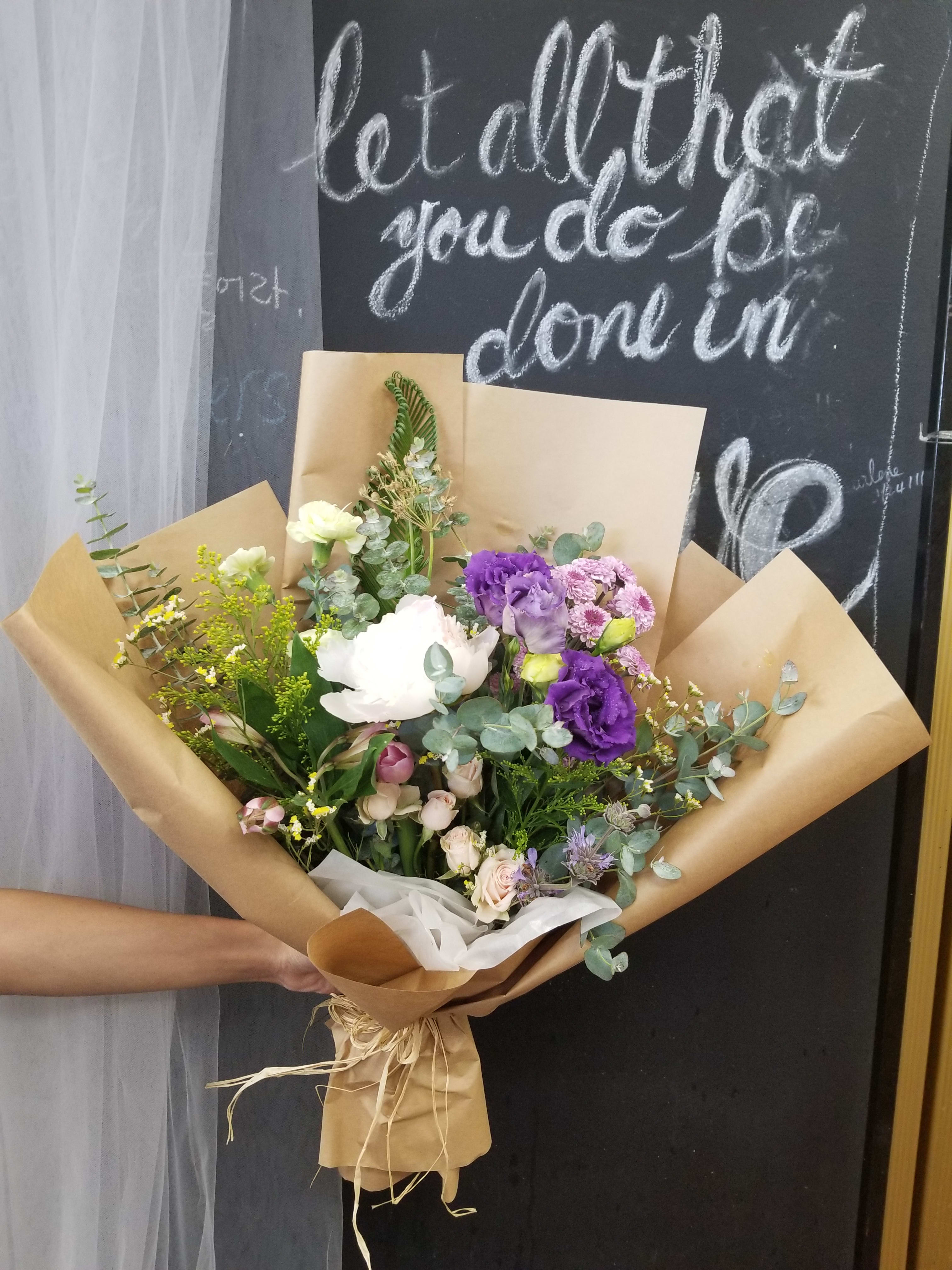 Hand-tied bouquet of purple, white, and pink flowers in brown paper
