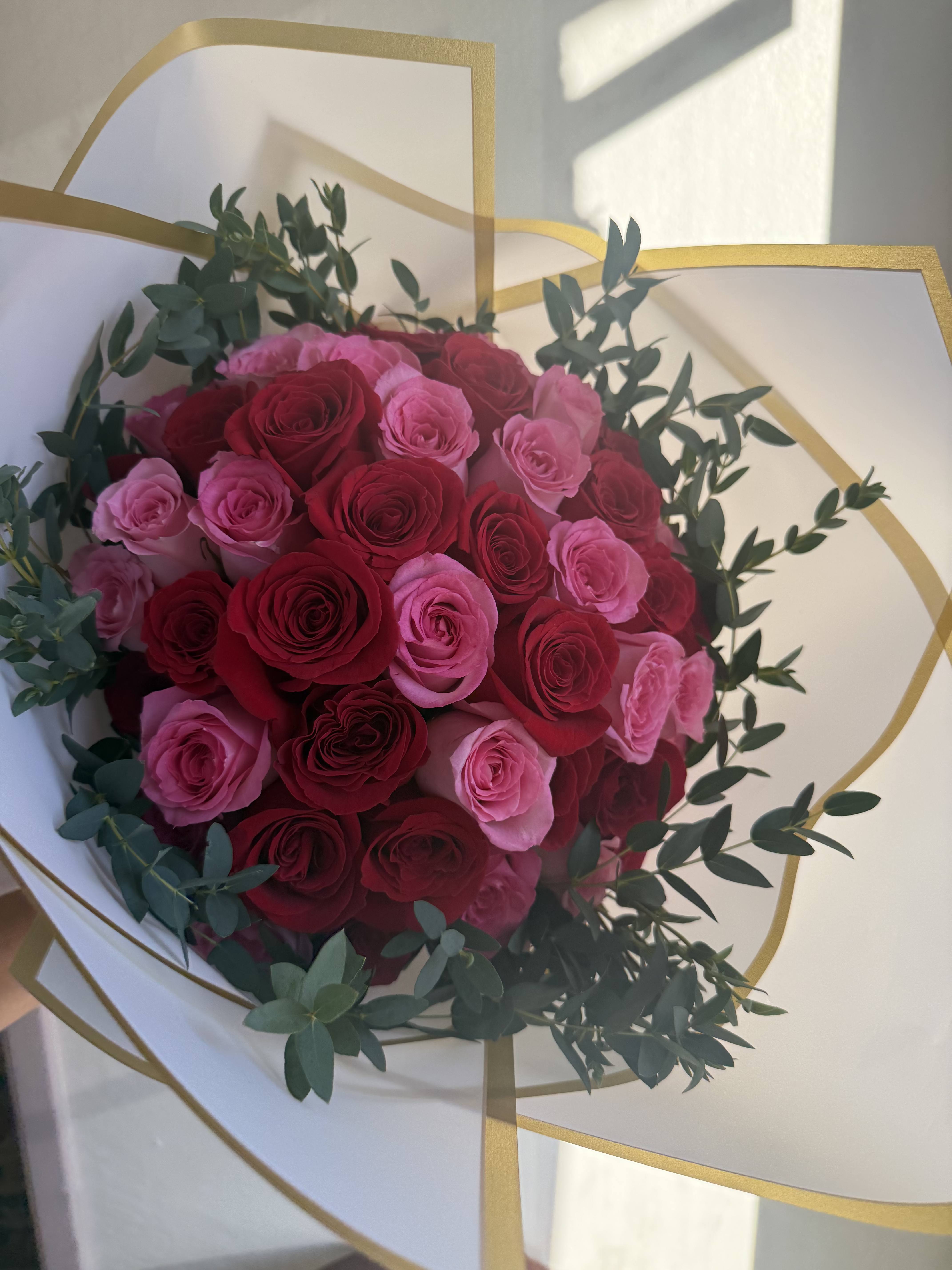 Round bouquet of red and pink roses wrapped in white paper with gold trim