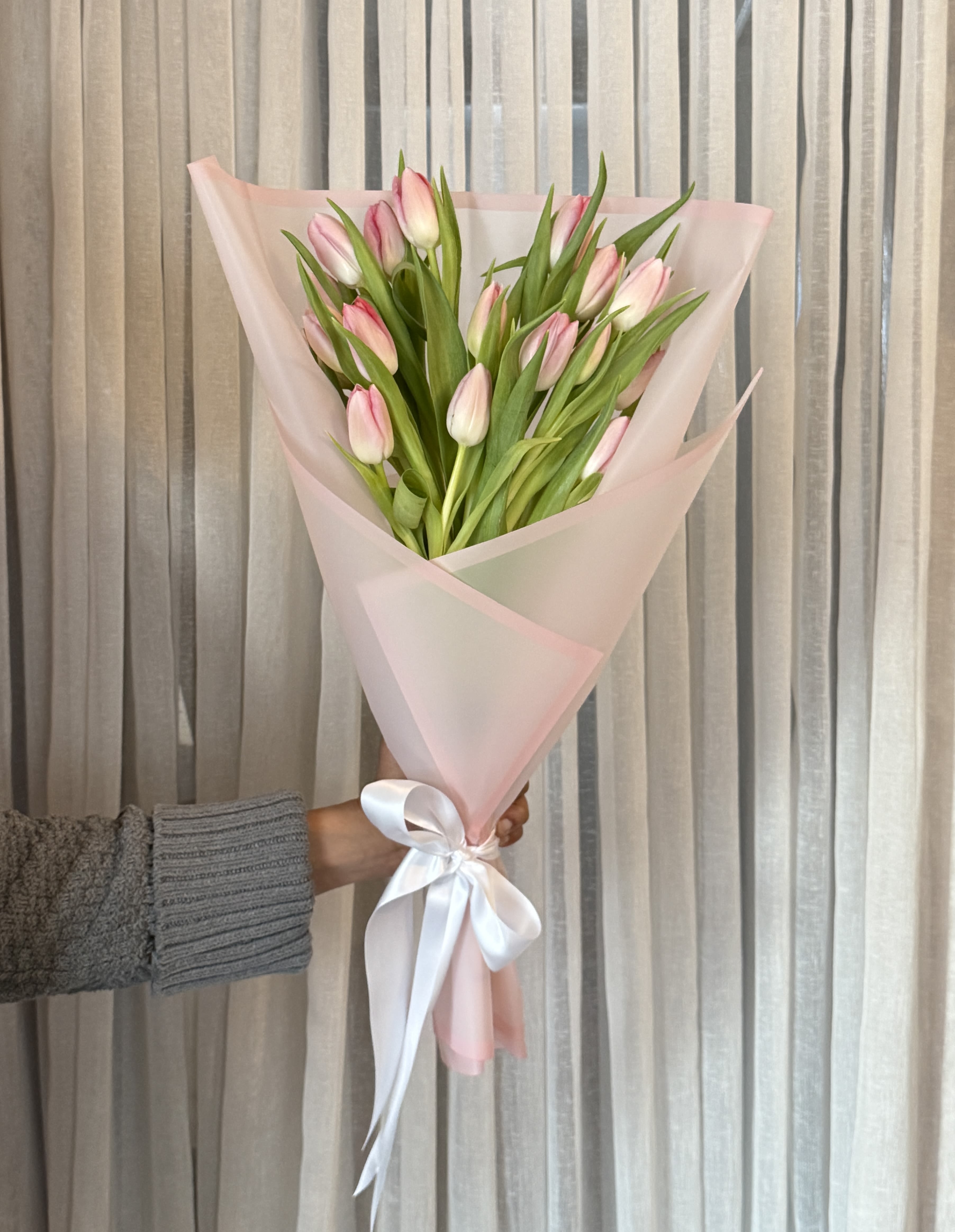 Pink tulip bouquet wrapped in pale pink paper with a white ribbon