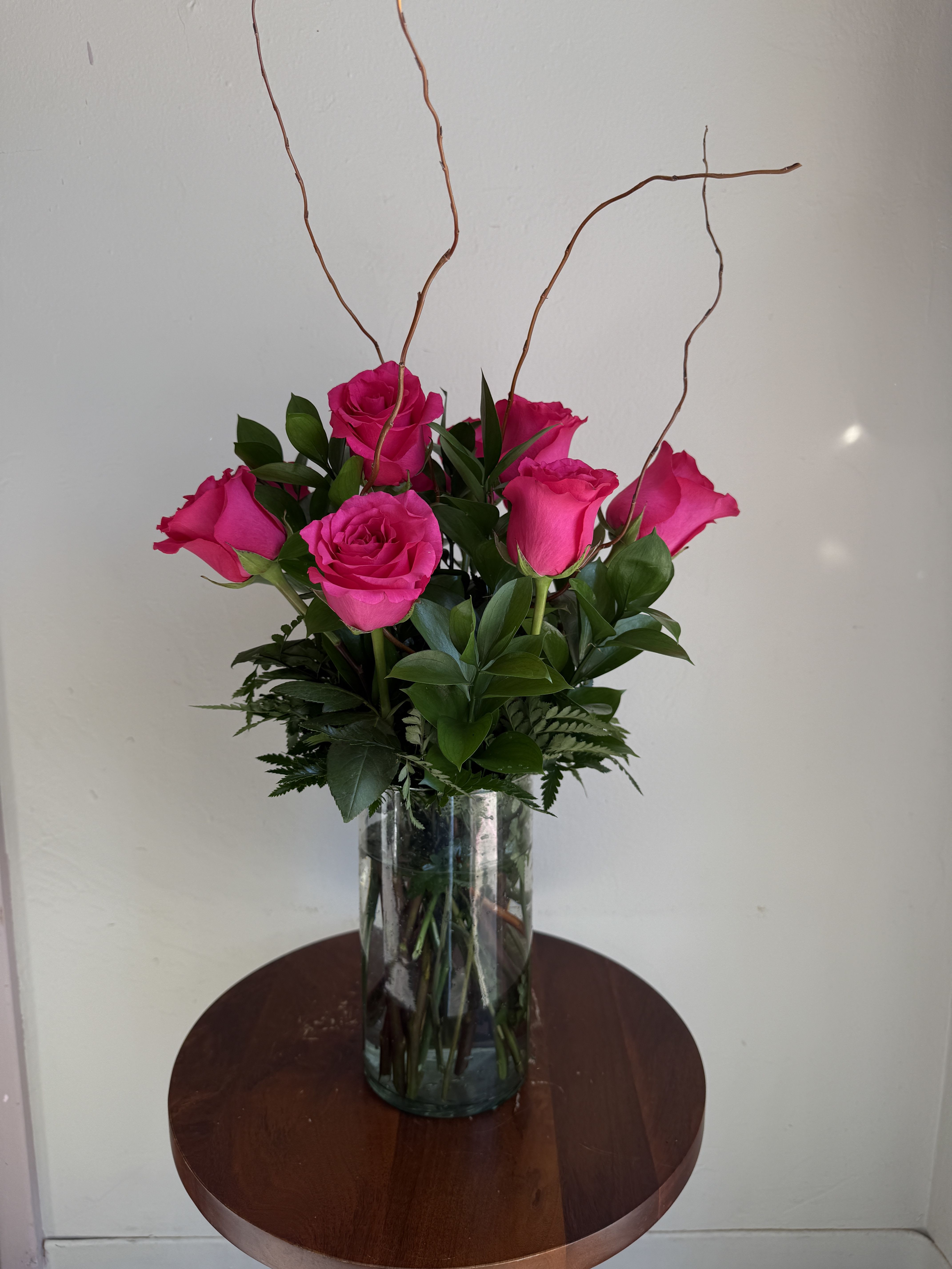 Pink roses arranged in a clear glass vase with tall curly branches