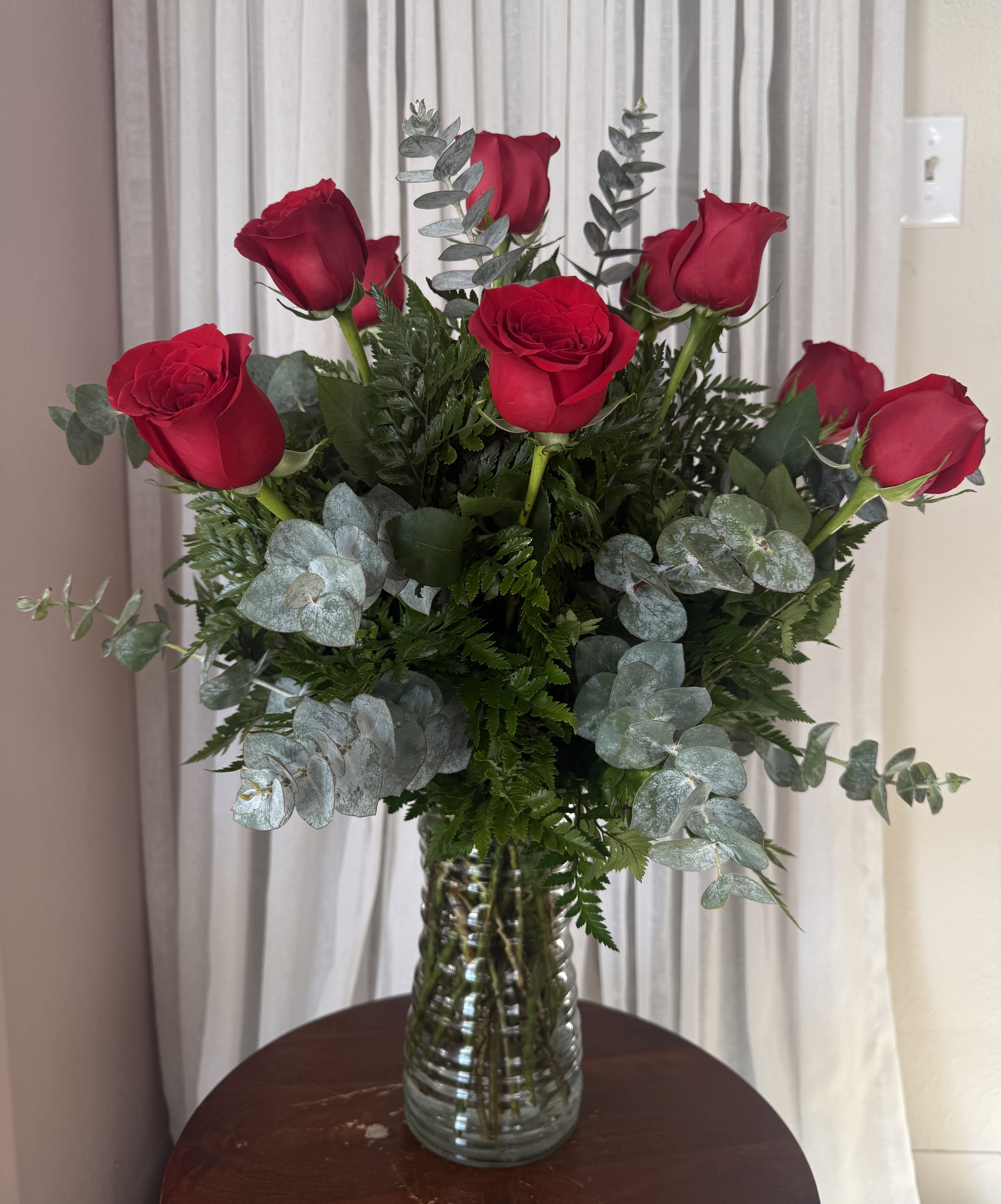 Red roses arranged in a clear glass vase with silvery eucalyptus