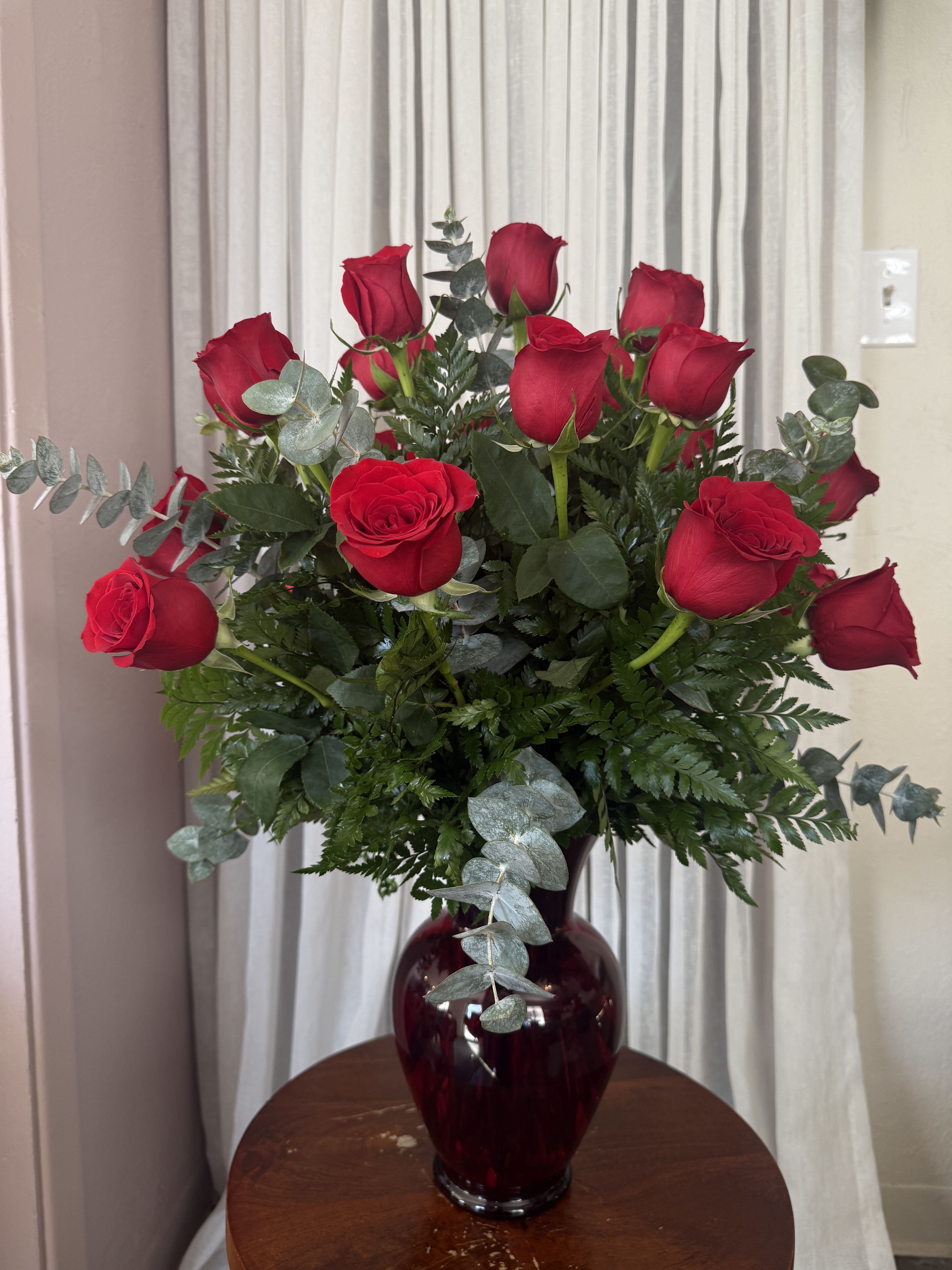 Red roses arranged in a dark glass vase with eucalyptus