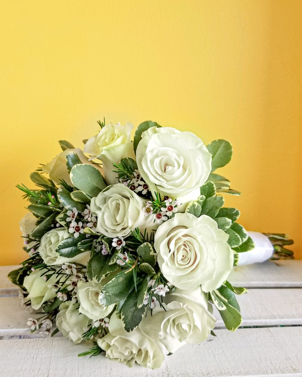 Bouquet of white roses with greenery on a yellow background