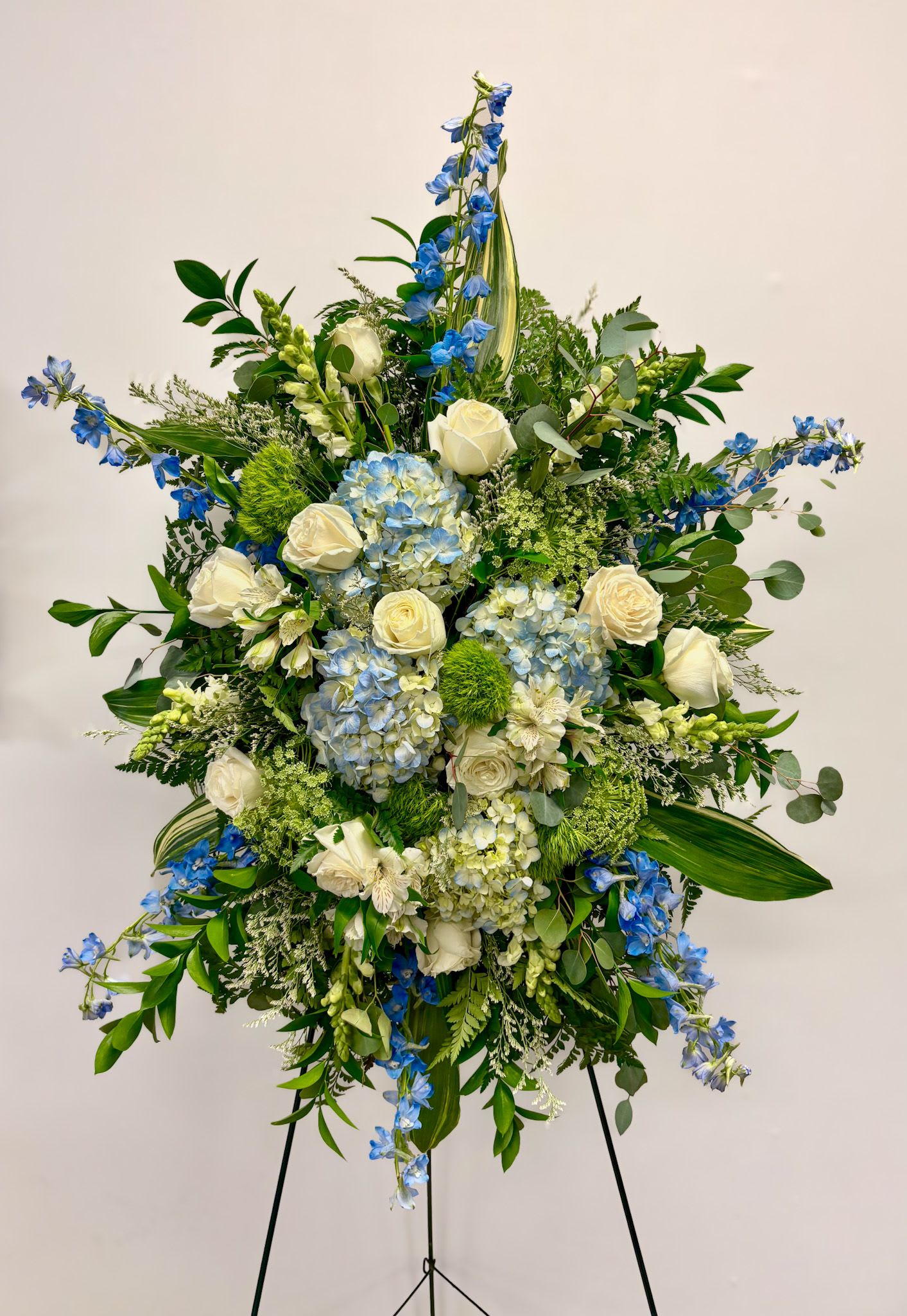 Peaceful Stream - This standing funeral spray includes blue hydrangea, delphinium, white roses, lace flower, alstromeria and limonium.
