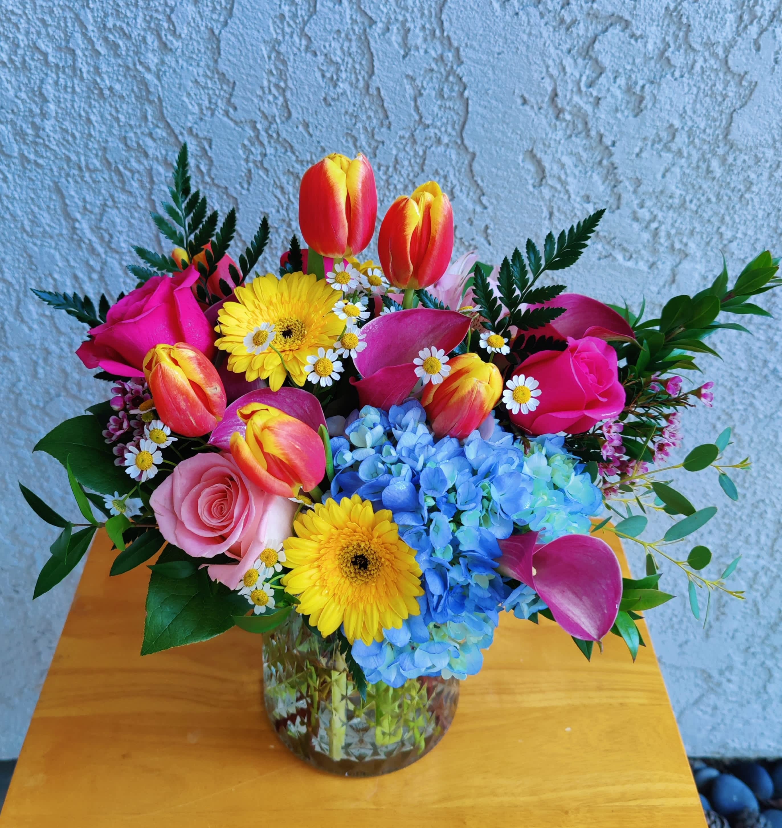 Colorful bouquet of tulips, roses, gerbera daisies, hydrangeas, and small daisies in a glass vase