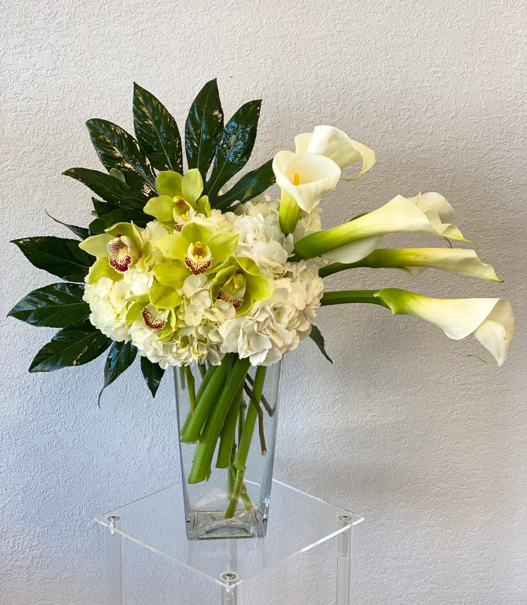 White calla lilies and green orchids in a clear glass vase