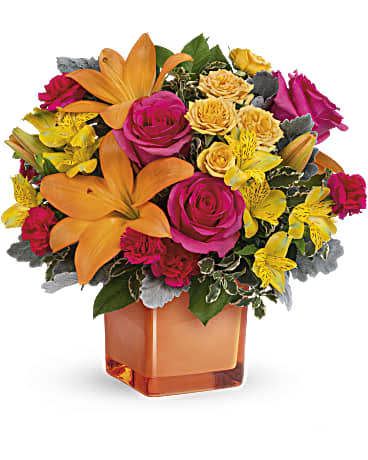 Bright bouquet of orange lilies, pink roses, and yellow flowers in an orange vase