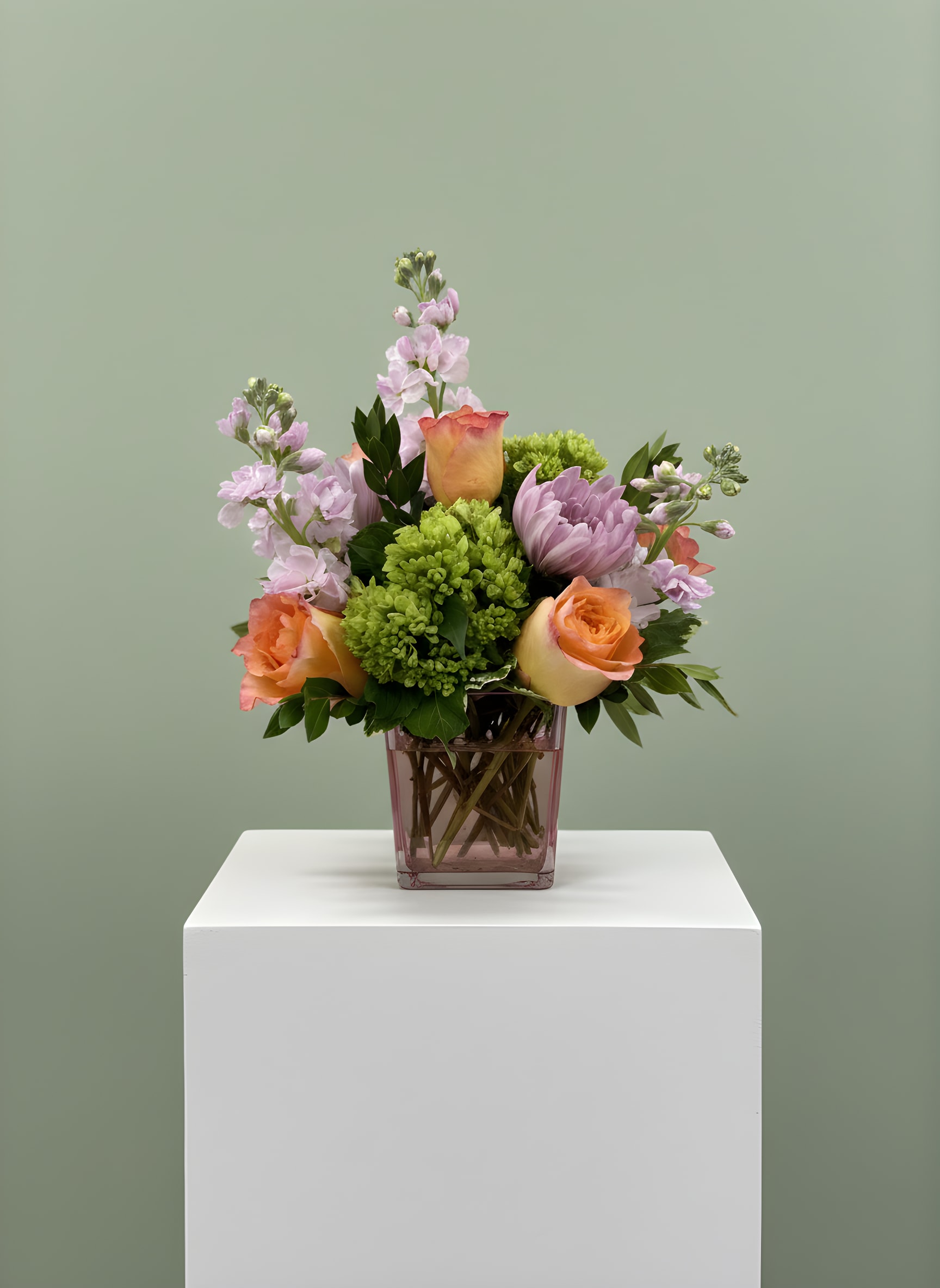 Mixed bouquet of peach roses, lavender blooms, and green flowers in a pink vase