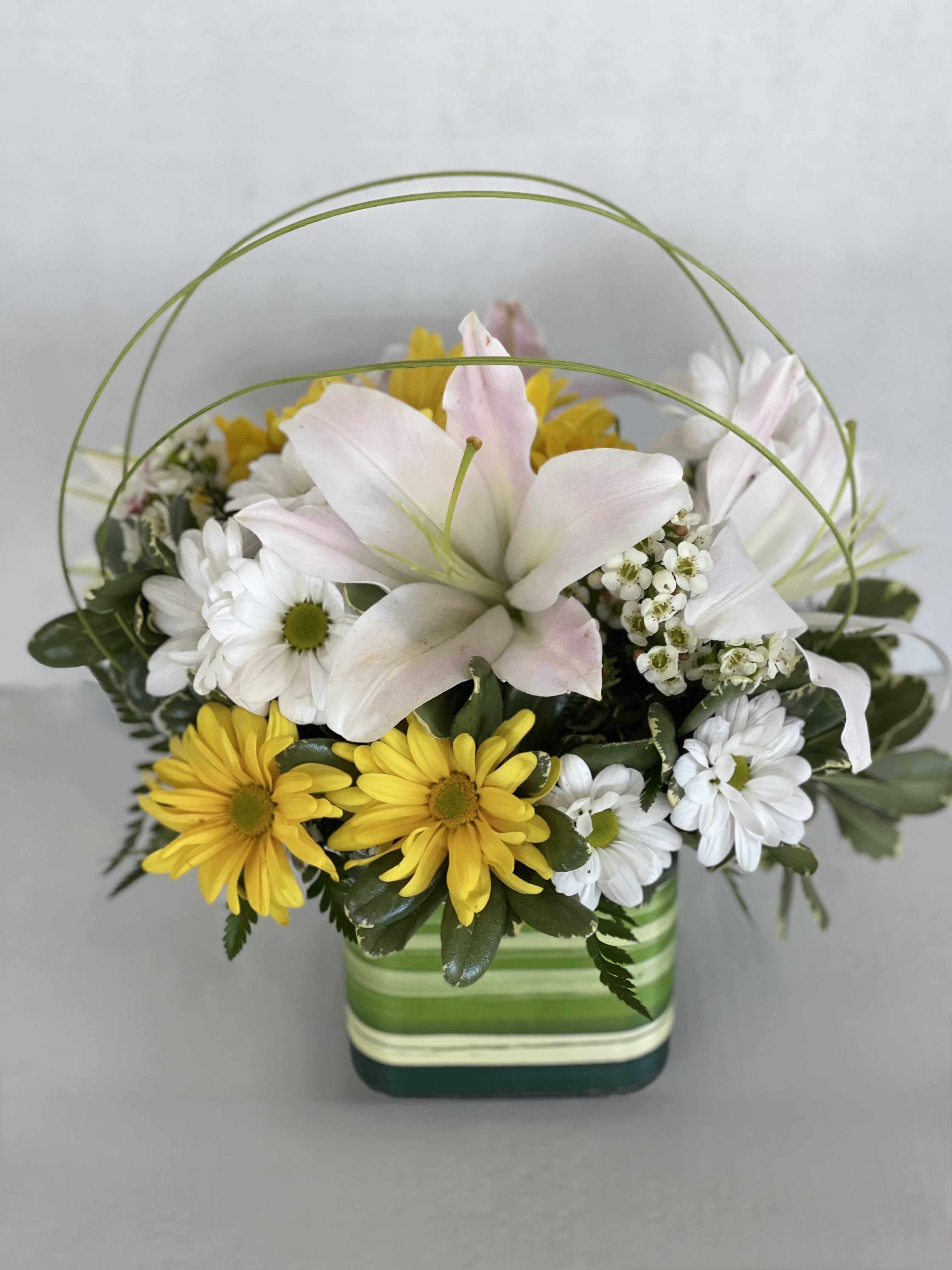 Mixed white and yellow flowers in a striped square vase with arched greenery