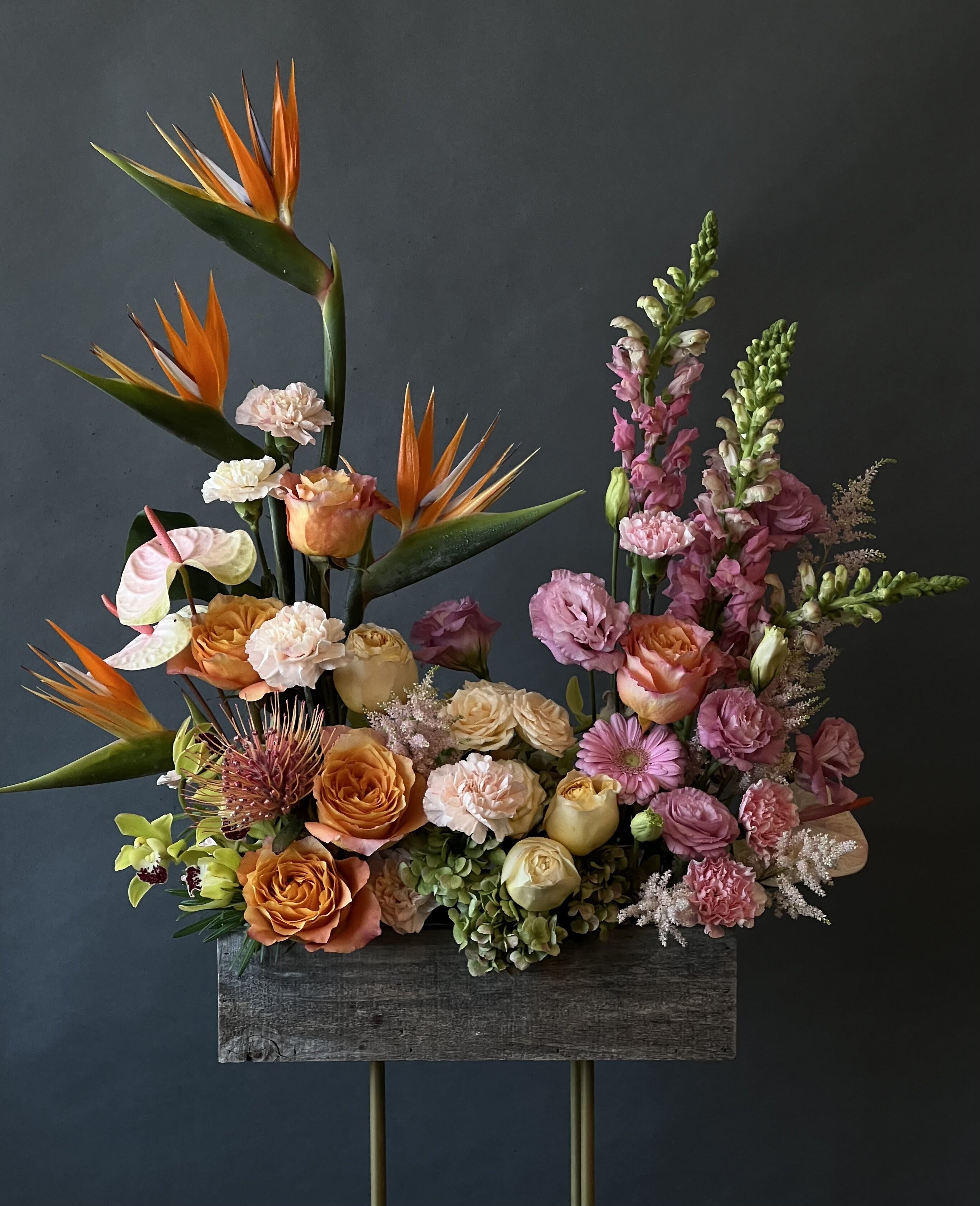 Tall floral arrangement with orange birds of paradise and pink roses in a wooden container