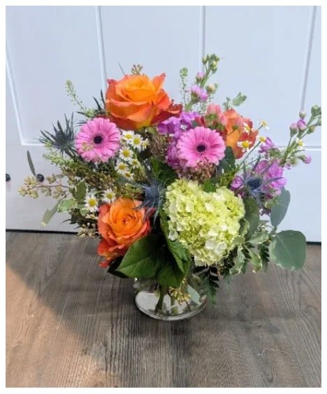 Free Your Spirit - Bright orange roses and pink gerbera daisies take center stage in this mixed-color birthday bouquet, Free Your Spirit, designed to make someone feel joyful and celebrated. The lively orange and soft pink paired with a pale green‑white hydrangea give the arrangement a fresh, garden-style energy-perfect for birthdays, thank-you gifts, or simply brightening a friend's day.  Set in a clear glass vase, the bouquet includes airy branching accents, small white daisy-like filler blooms, and subtle purple highlights for texture and movement. The loose, hand-arranged silhouette lets stems breathe rather than sit tightly packed, offering a casual, natural charm that reads as cheerful and approachable.  Give this to the person you want to lift up-she'll feel noticed and cared for the moment the colors catch her eye. Available in one standard vase size; replace vase water every 2-3 days, trim stems at an angle if desired, and keep away from direct heat to extend freshness.