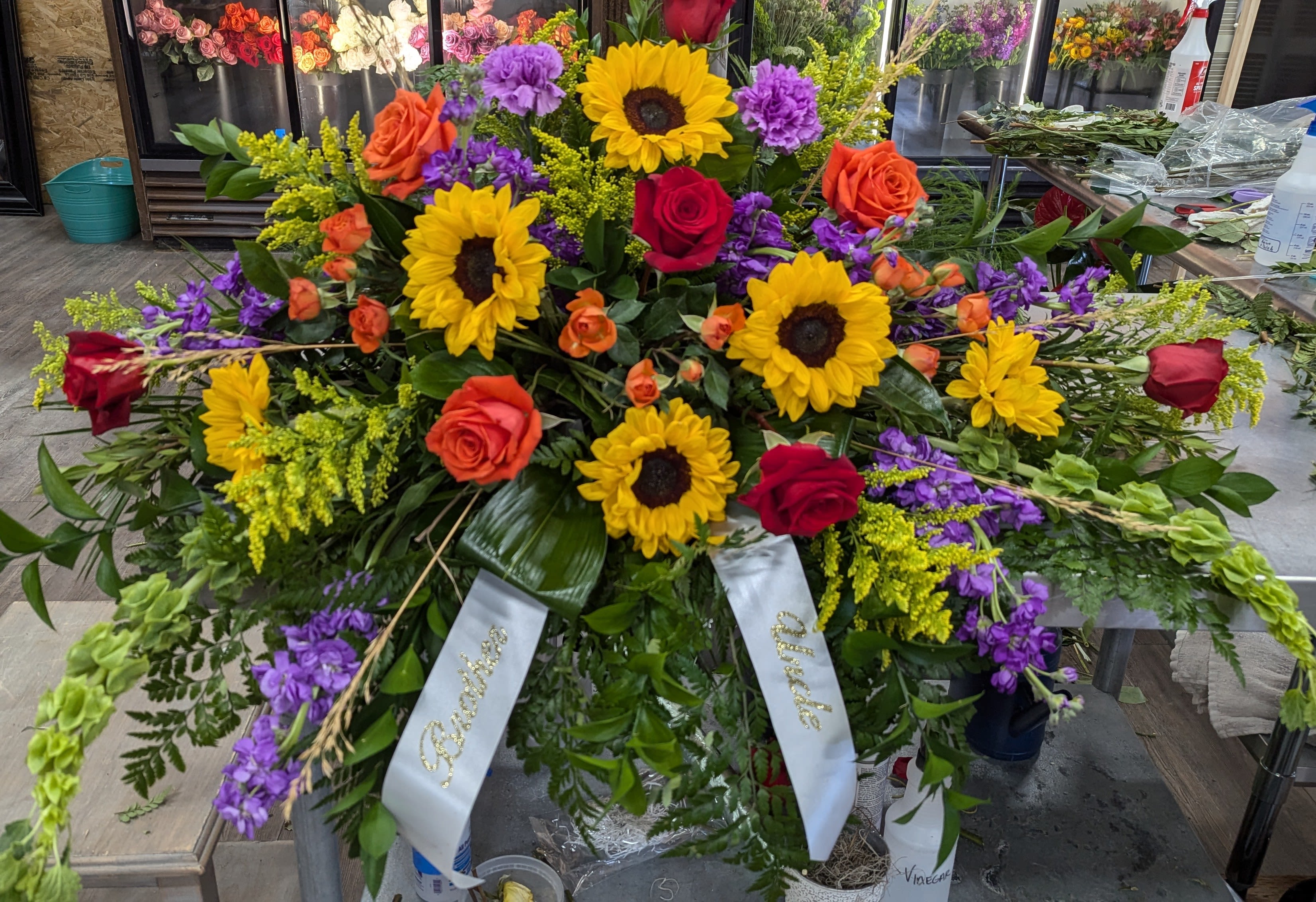 Colorful Reflections casket Spray - Casket spray includes Red and Orange Roses, Sunflowers, Carnations, Stock, Bells of Ireland and greenery. Choose your color palette and price point. 