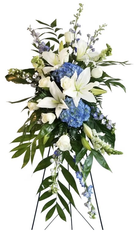 Standing floral spray with white lilies, blue hydrangeas, and an easel