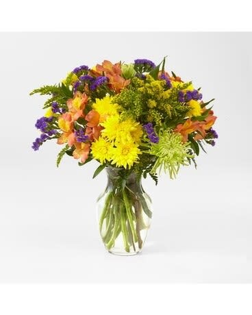 Mixed bouquet of yellow, orange, and purple flowers in a clear glass vase