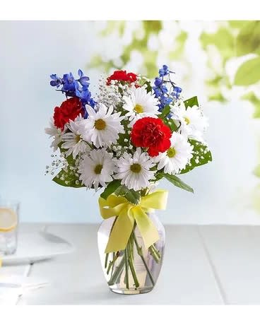 Bouquet of red, white, and blue flowers in a glass vase with a yellow ribbon