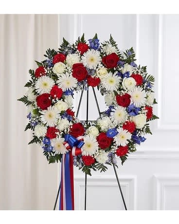 Circular wreath of red, white, and blue flowers on a stand with ribbon