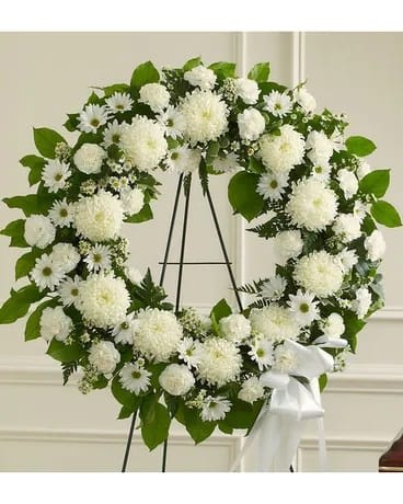 White floral wreath on a black stand with a white ribbon