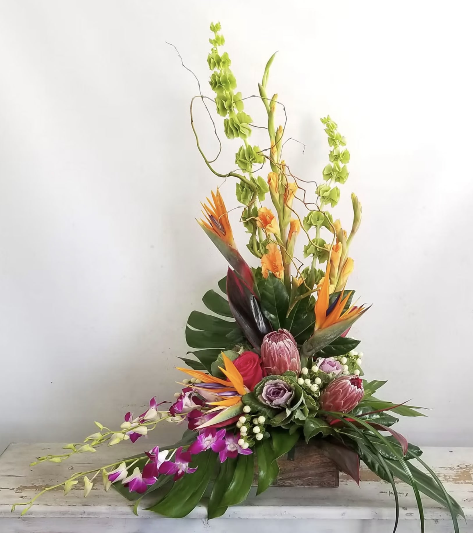 Tall tropical flower arrangement with orange bird-of-paradise and orchids in a wooden container