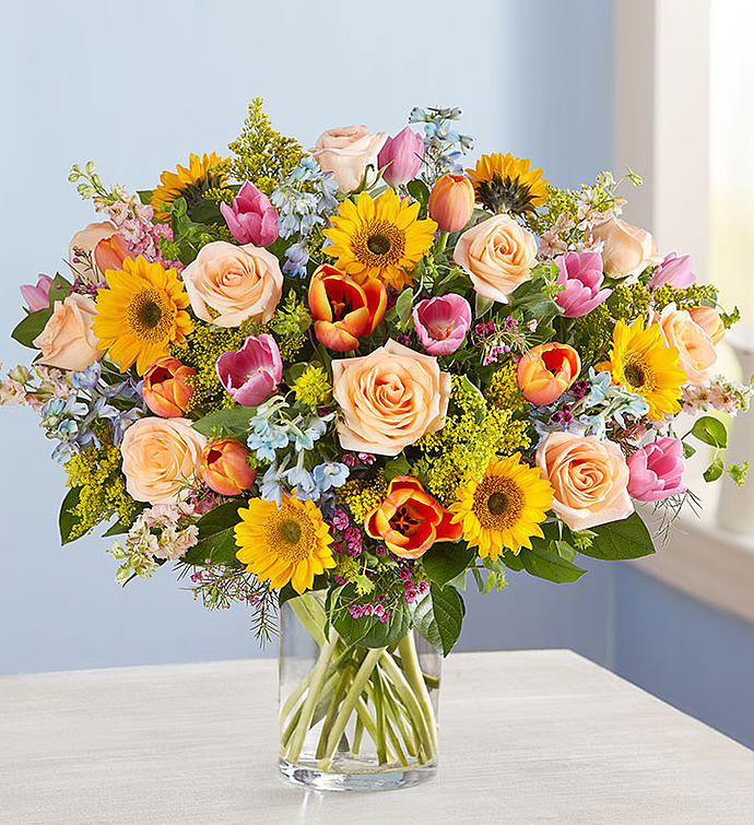Mixed bouquet of roses, tulips, and sunflowers in a clear glass vase