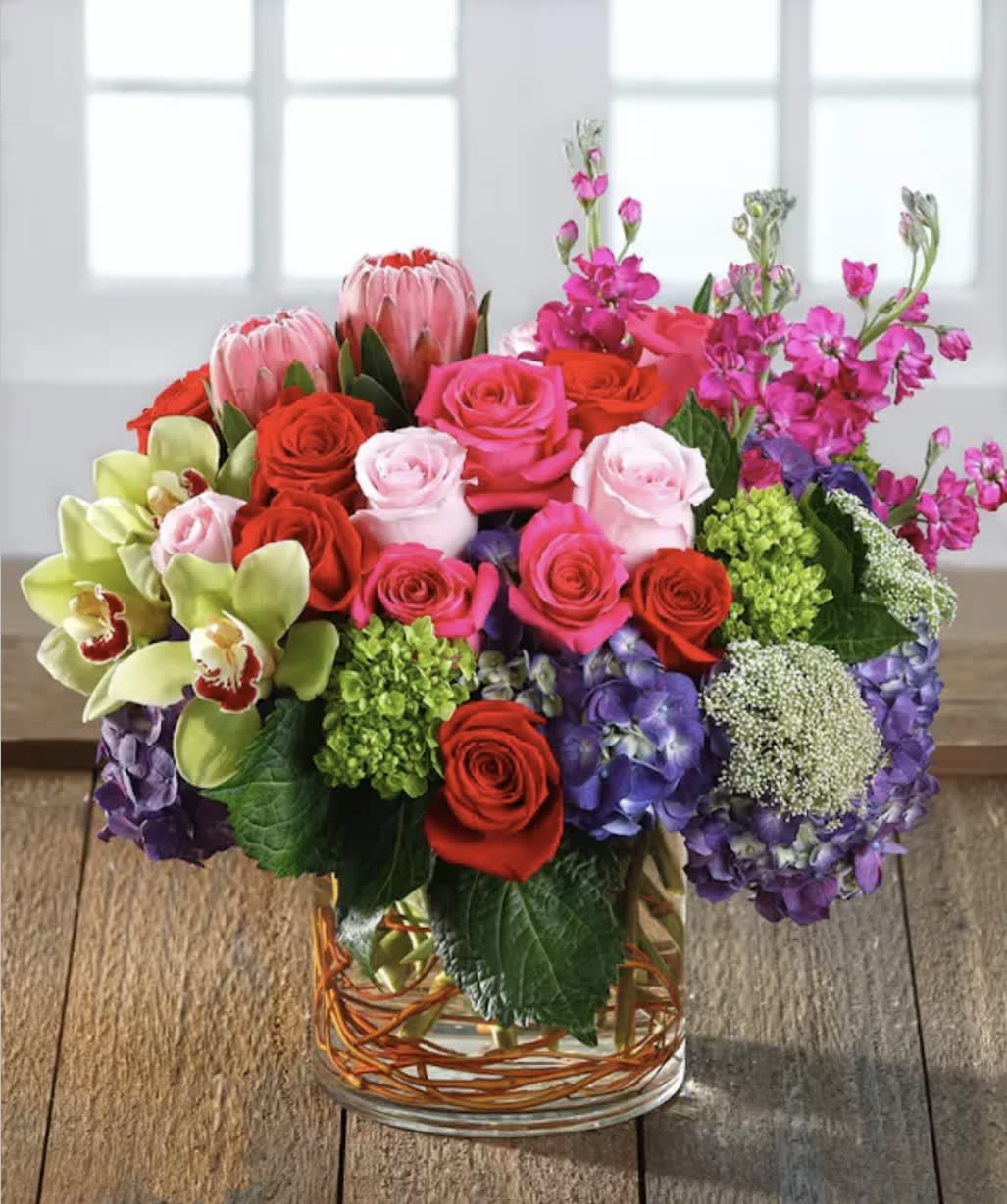 Mixed bouquet of roses, orchids, hydrangeas, and protea in a glass vase