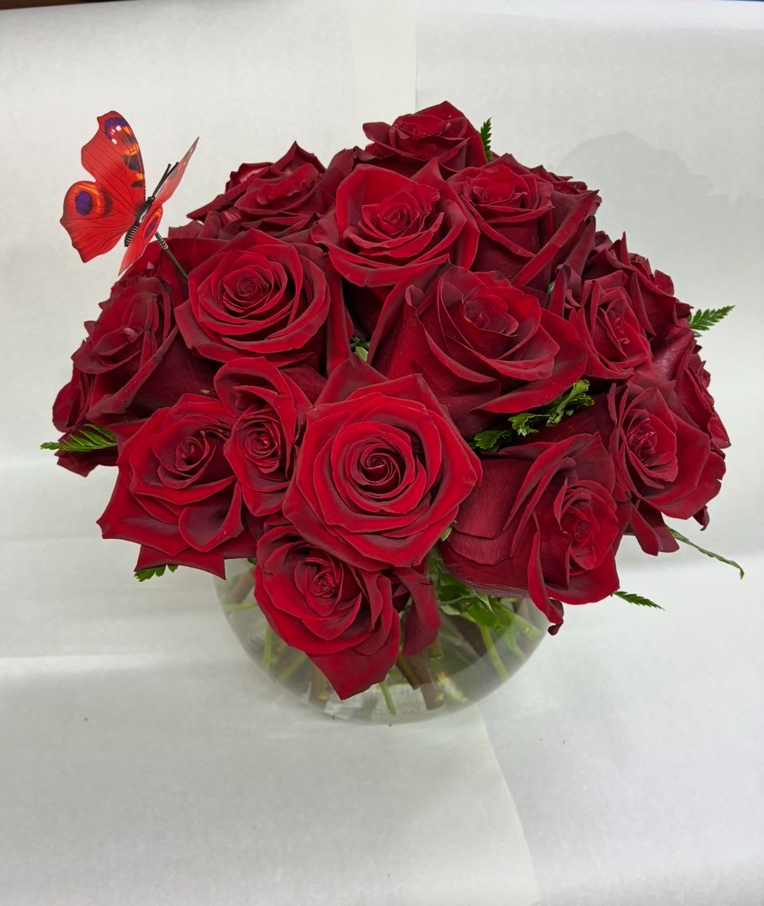 Bouquet of red roses in a clear glass vase with a butterfly pick