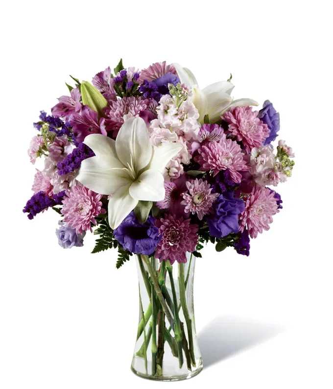 Purple and pink mixed bouquet with white lilies in a clear glass vase