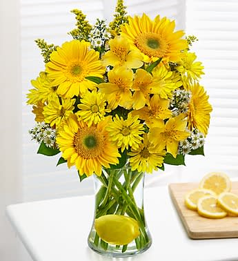 Make Lemonade in a Vase - Product ID: 91356  For everyone out there who likes to look on the bright side, this bouquetâs for you! Cheerful yellow Gerbera daisies, alstroemeria, daisy poms and more are hand-designed by our expert florists in a glass gathering vase with a real lemon for a truly original twist that keeps the smiles coming. An added box of a delicious chocolate sweetens this one-of-a-kind gift. Bright bouquet of Gerbera daisies, alstroemeria, daisy poms, solidago, monte casino and salal Artistically designed by our select florists in a striking glass gathering vase; measures 8"H Features a festive twist of a fresh lemon in the vase Paired with an 8 oz. box of chocolate; assortment may vary due to local availability Large arrangement measures approximately 16.5"H x 13"L Medium arrangement measures approximately 16"H x 12"L Small arrangement measures approximately 15.5"H x 11"L Our florists hand-design each arrangement, so colors, varieties, and container may vary due to local availability
