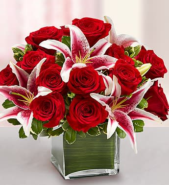 Modern Embrace Red Rose and Lily Cube - Product ID: 90973   She's always looking for the latest styles and hottest fashion trends. Send this truly original, contemporary bouquet of gorgeous red roses and elegant lilies, hand-arranged in a stylish glass cube vase, and she'll think it's the perfect accessory for her modern sensibility. Hand-crafted arrangement of romantic roses and lilies, accented by variegated pittosporum Designed by our expert florists in a modern clear glass cube vase wrapped with an exotic ti leaf; vase measures 5"H Large arrangement measures approximately 14"H x 14"L Medium arrangement measures approximately 12"H x 12"L Small arrangement measures approximately 10"H x 10"L Our florists hand-design each arrangement, so colors, varieties, and container may vary due to local availability Lilies may arrive in bud form and will open to full beauty over the next 2-3 days