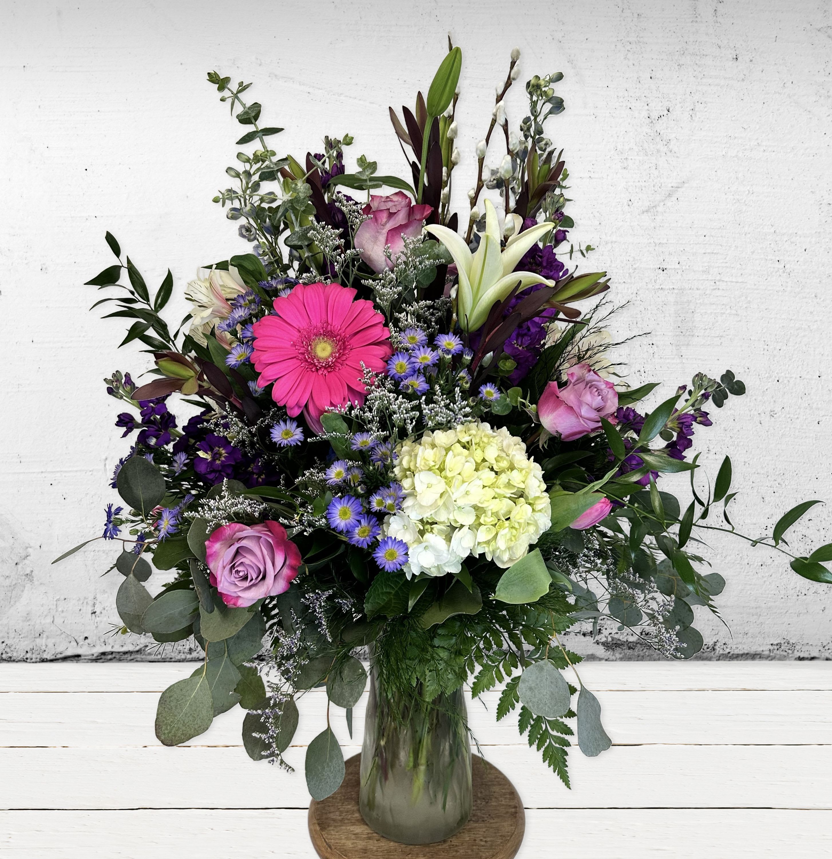 Tall mixed bouquet of pink gerbera, roses, white lilies and green hydrangea in a clear glass vase