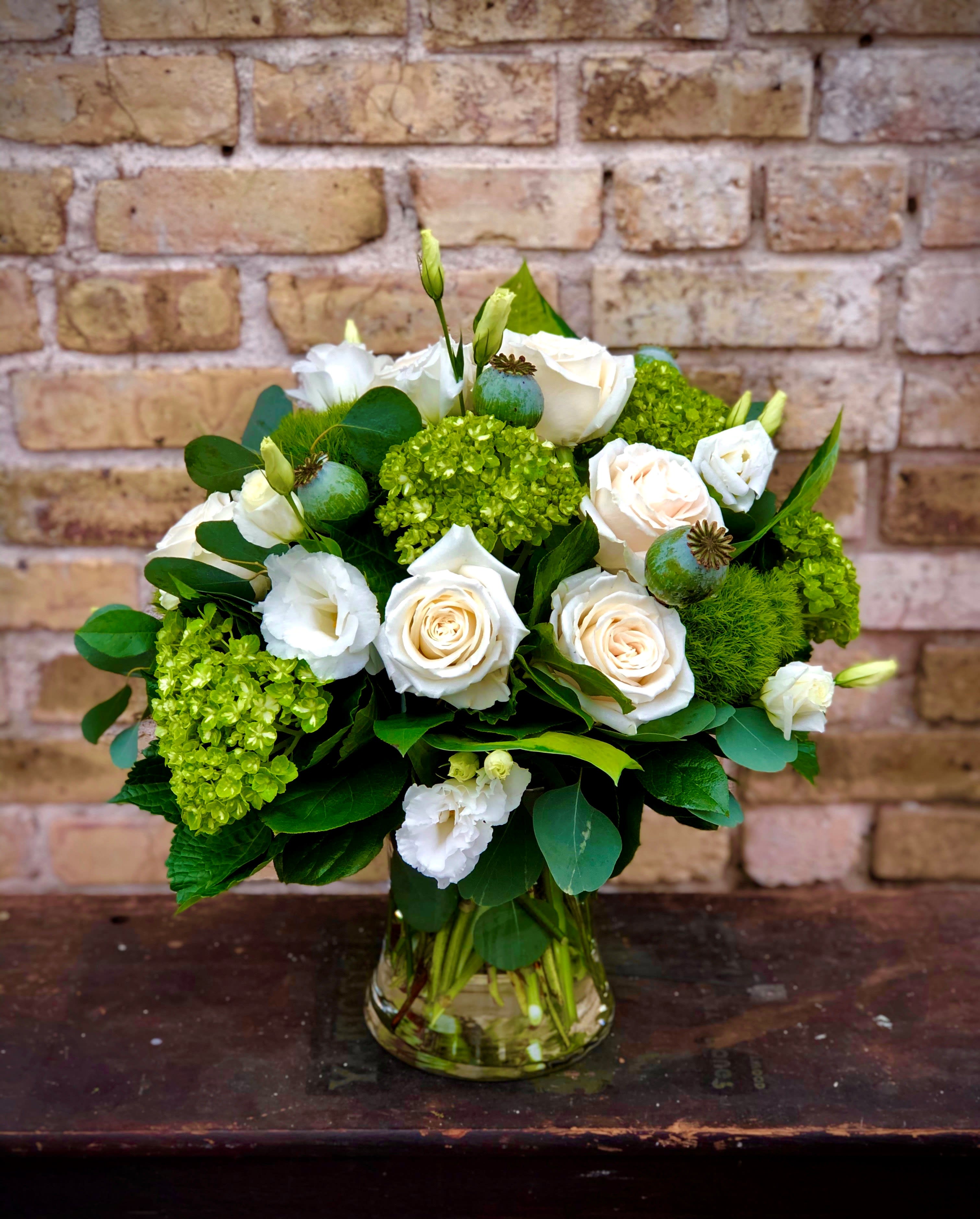 White roses and green blooms arranged in a glass vase