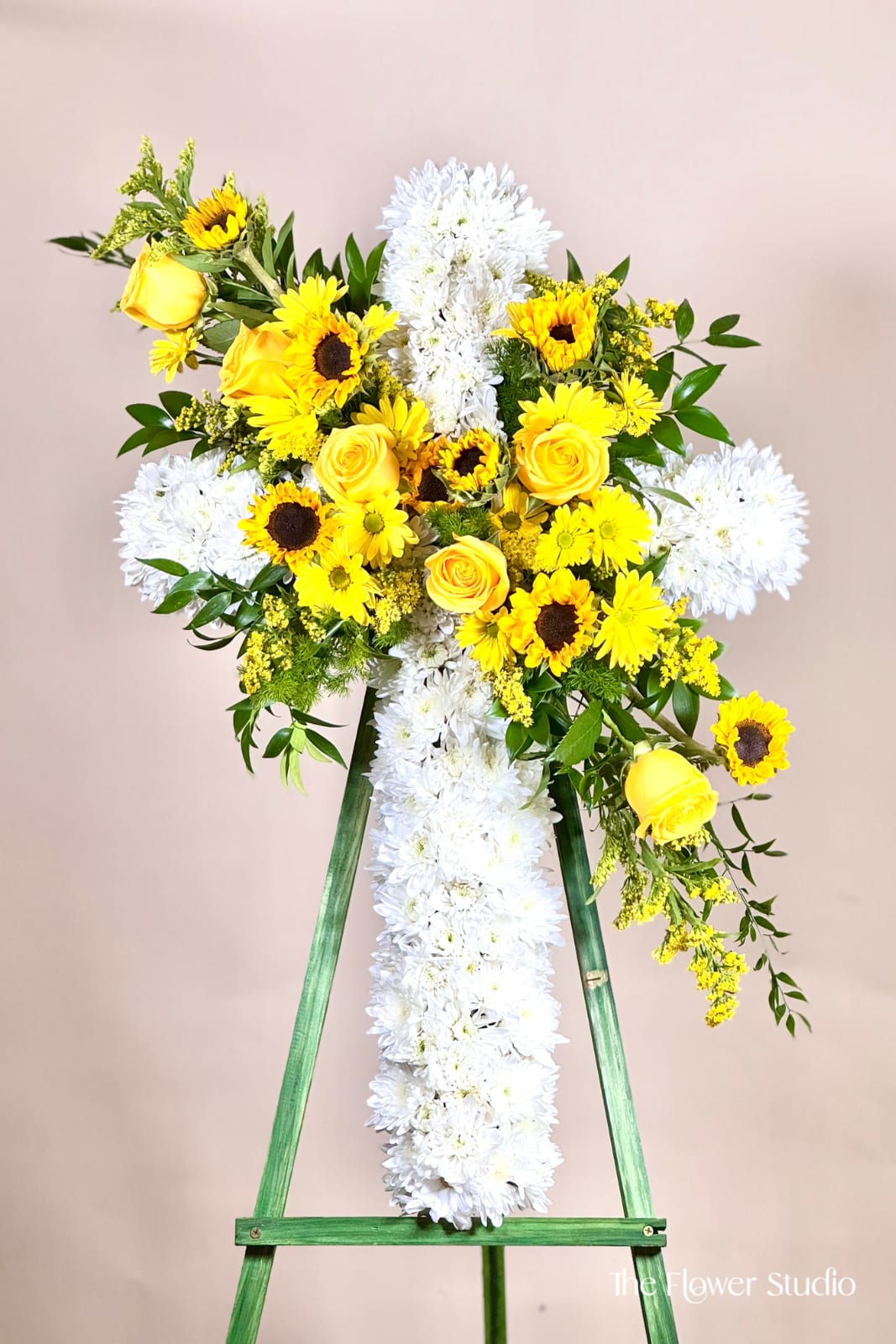 Yellow roses and sunflowers arranged on a white floral cross easel.
