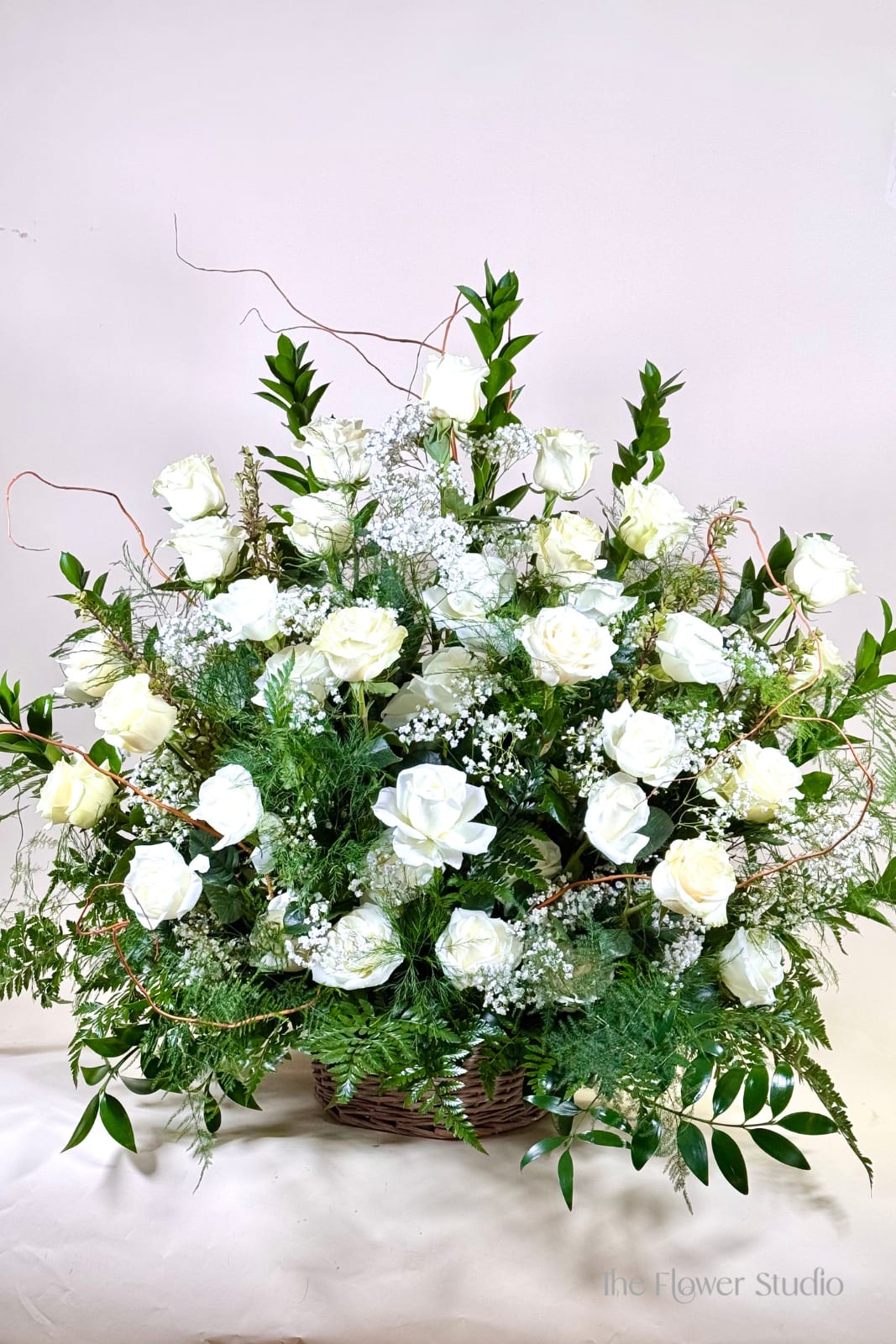 Large white rose arrangement in a wicker basket with greenery