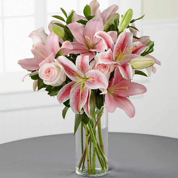 Pink lilies and roses arranged in a clear glass vase