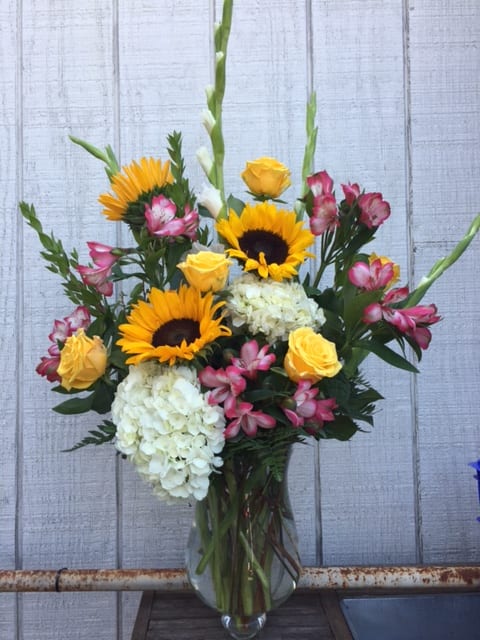 Bouquet of sunflowers, yellow roses, white hydrangeas, and pink alstroemeria in a glass vase