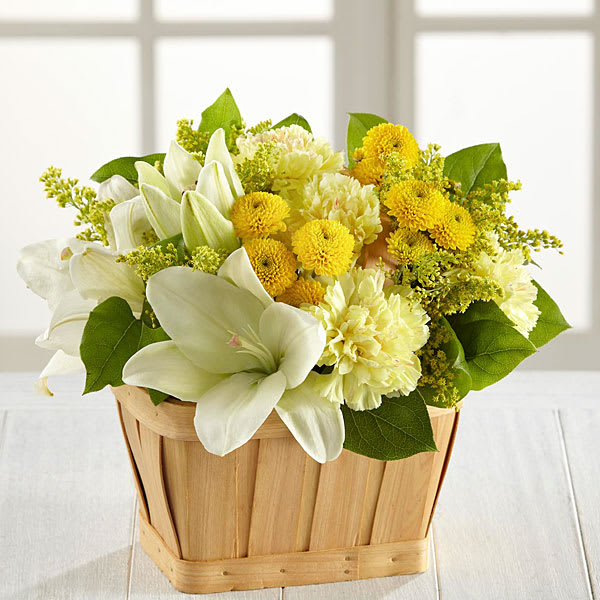 White lilies and yellow flowers arranged in a wooden basket