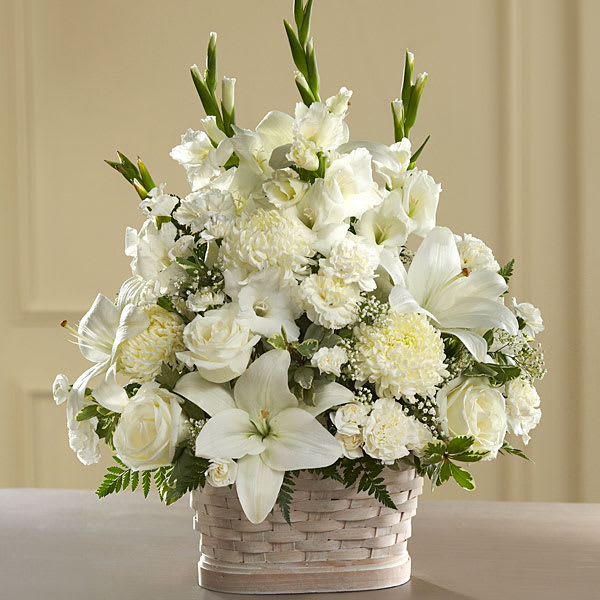 White floral arrangement in a woven basket with lilies and roses