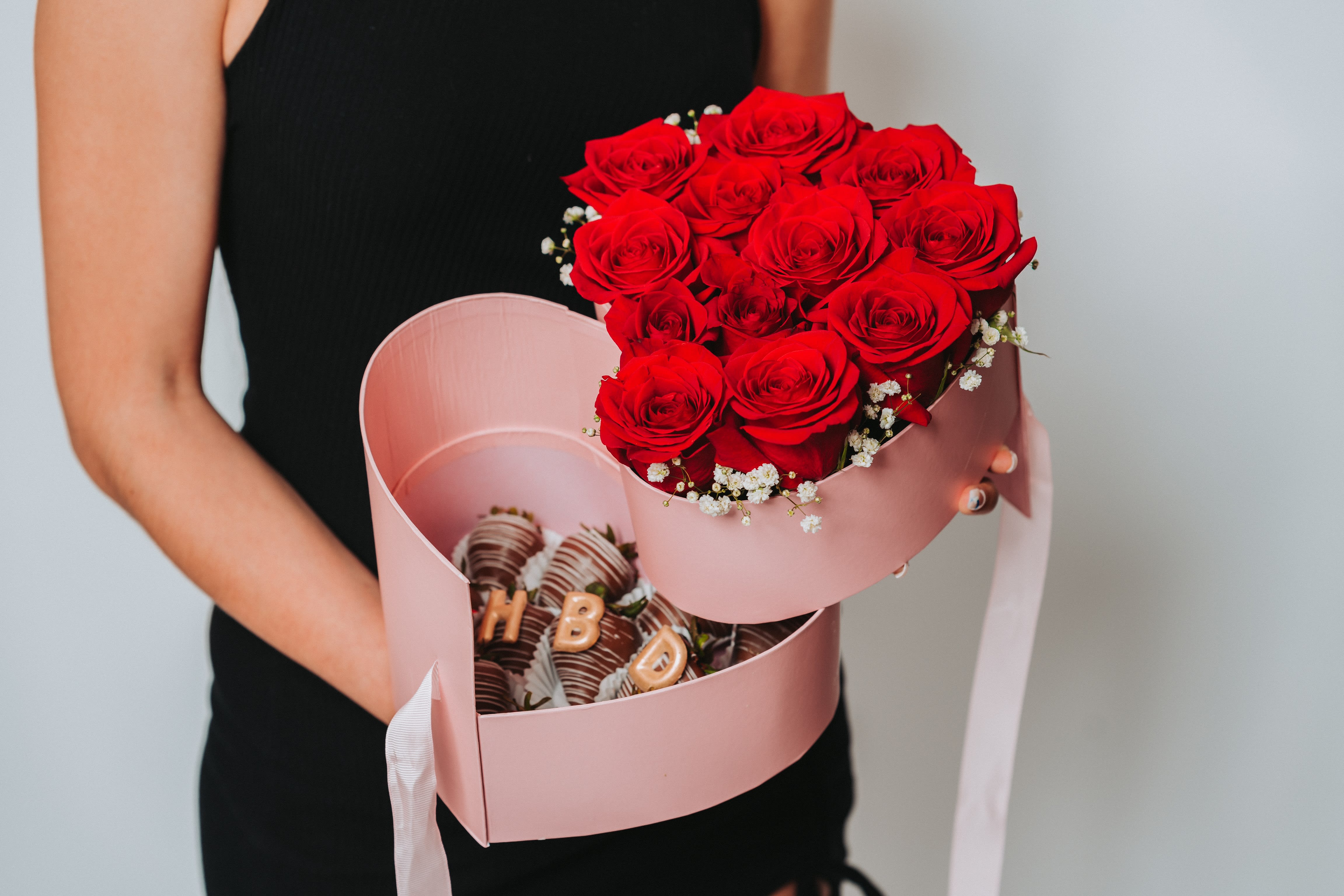 Woman holding a pink heart-shaped box with red roses and chocolate-covered strawberries