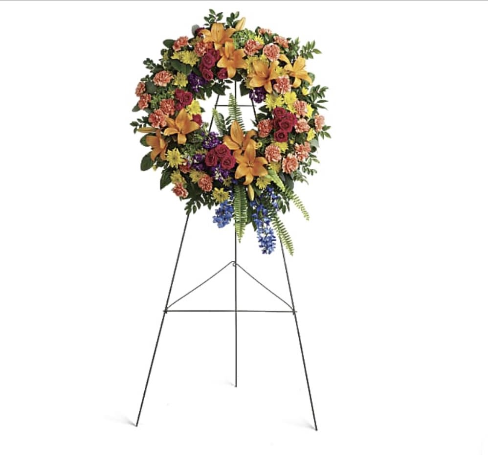 Large floral wreath on a standing easel with mixed orange, pink, purple, and yellow flowers