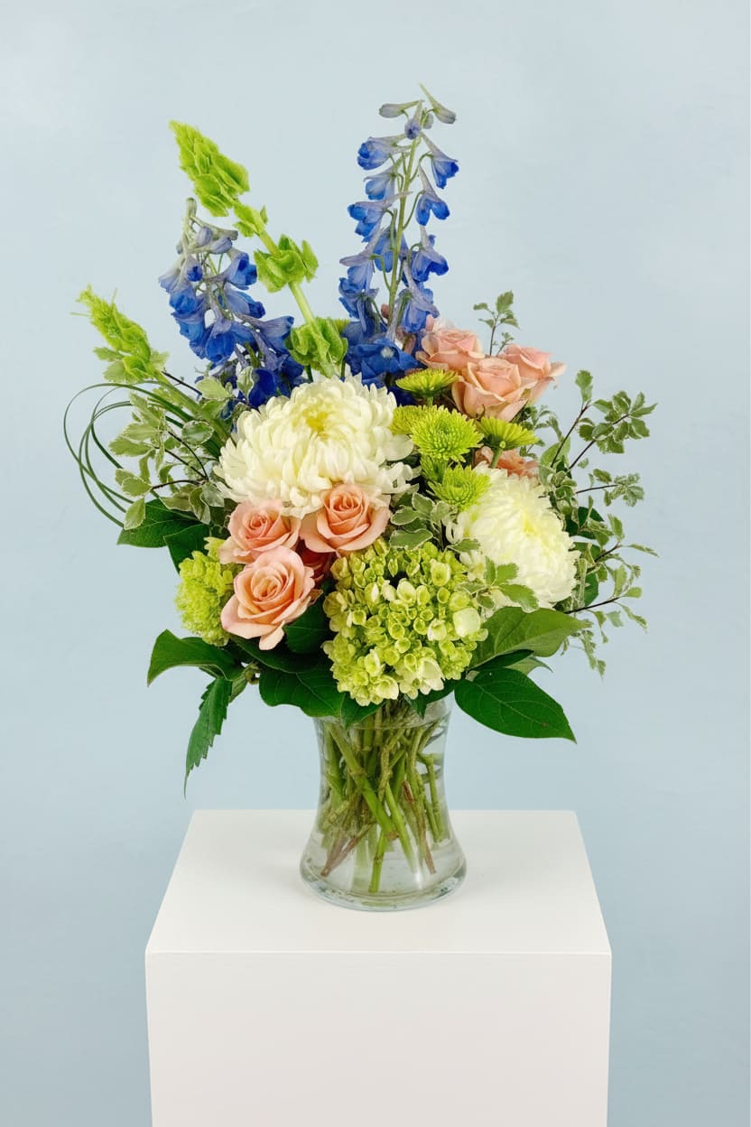 Mixed bouquet in a clear glass vase with blue, peach, and white blooms