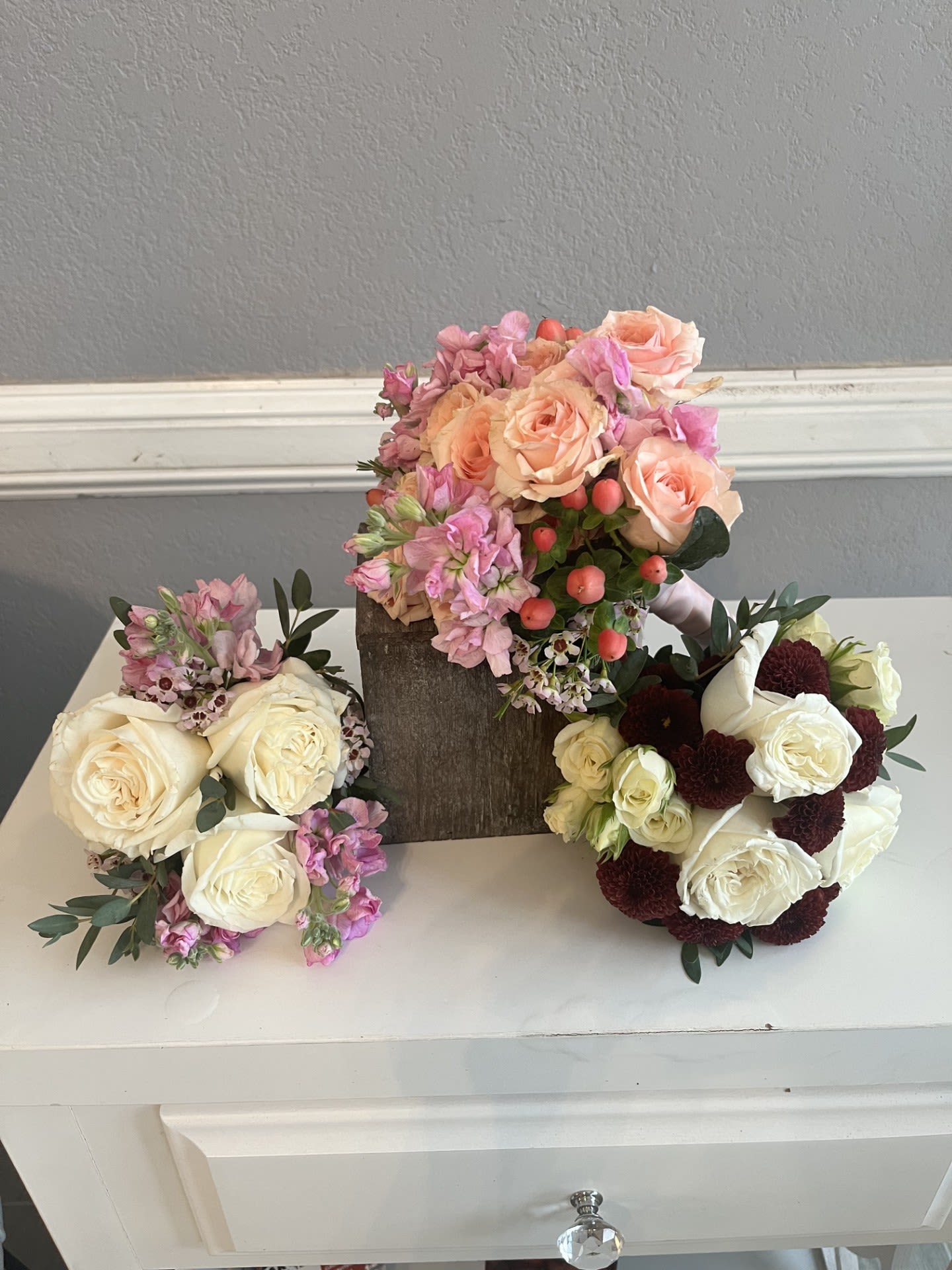 Three floral bouquets with roses and pink blooms arranged on a white surface