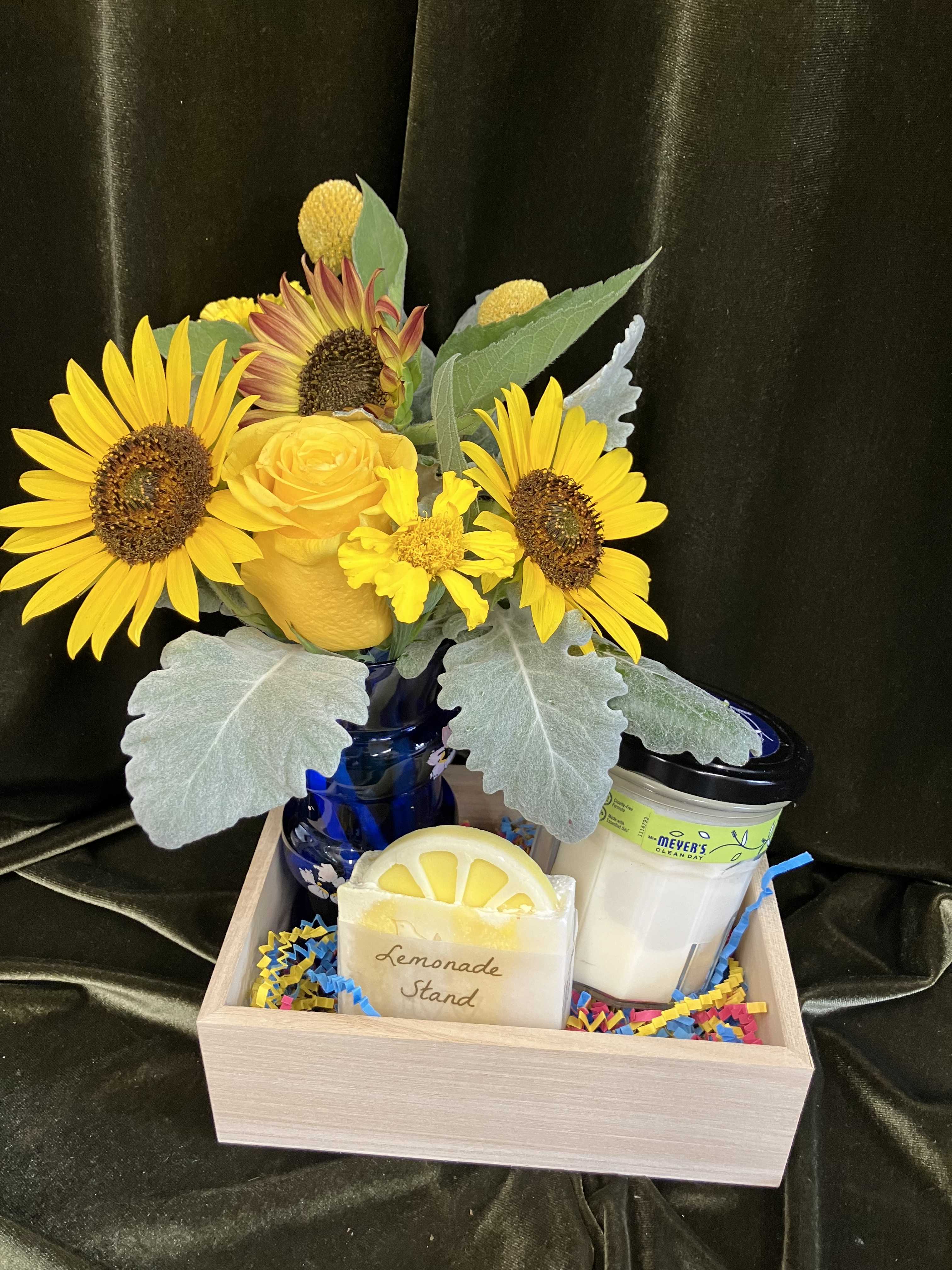 Sunflower bouquet in a blue vase with a lemon-shaped candle and a soap jar in a wooden tray.