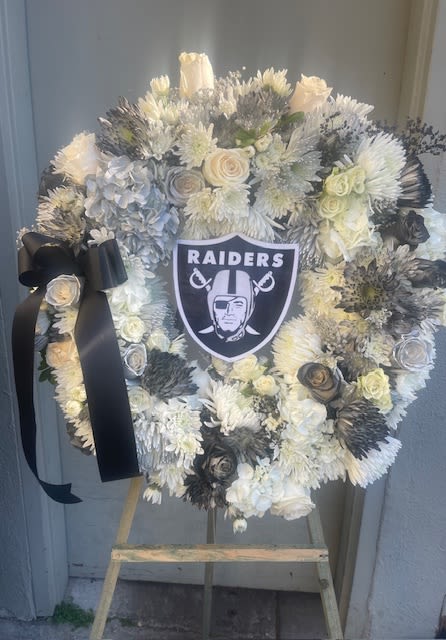 Heart-shaped white floral wreath with a Raiders emblem and black ribbon