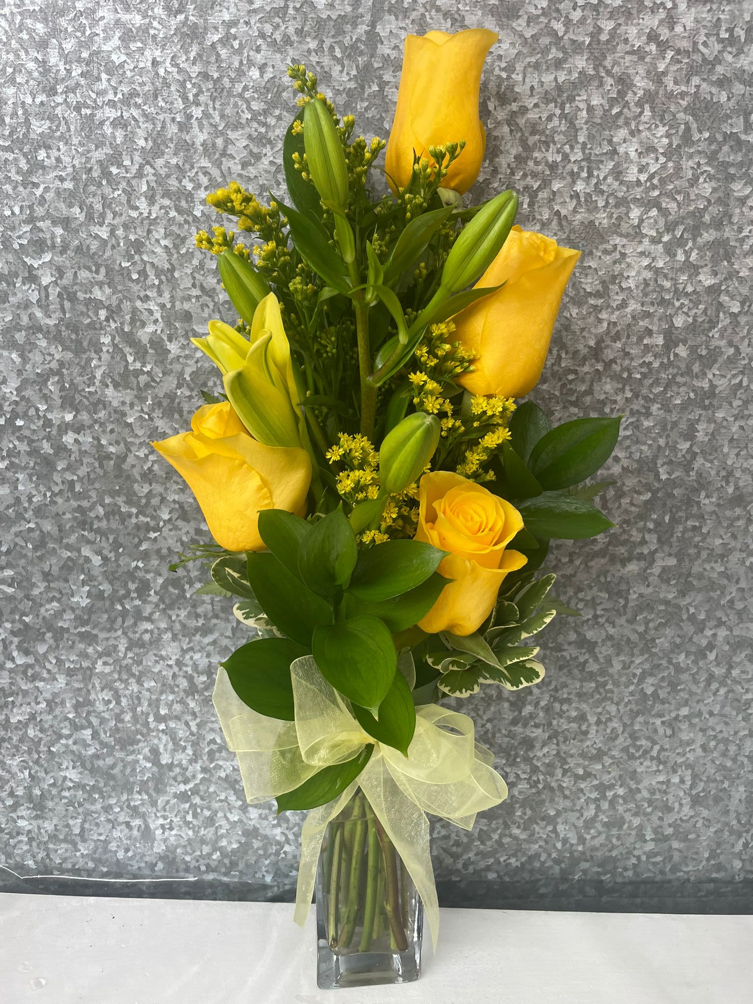 Yellow roses and lilies in a clear glass vase with a ribbon