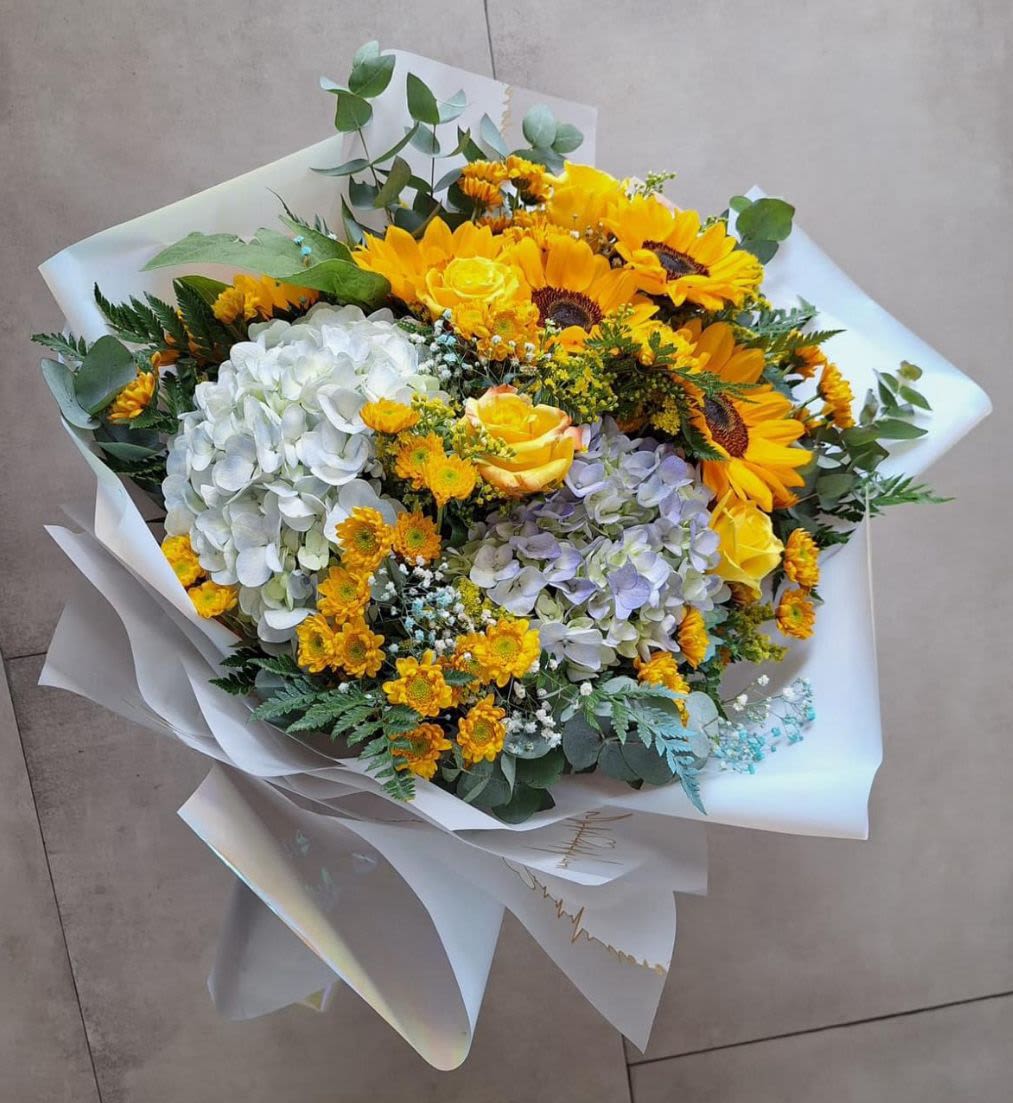 Bouquet of sunflowers, hydrangeas, and yellow roses wrapped in white paper