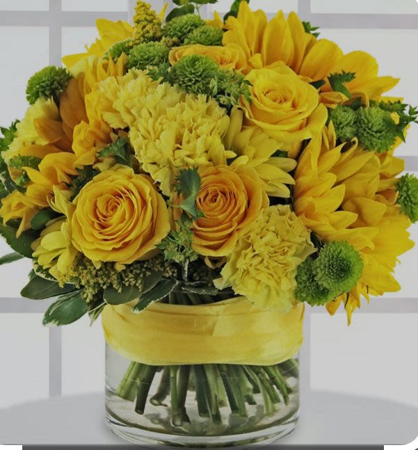 Yellow roses and sunflowers arranged in a glass vase with a yellow ribbon.